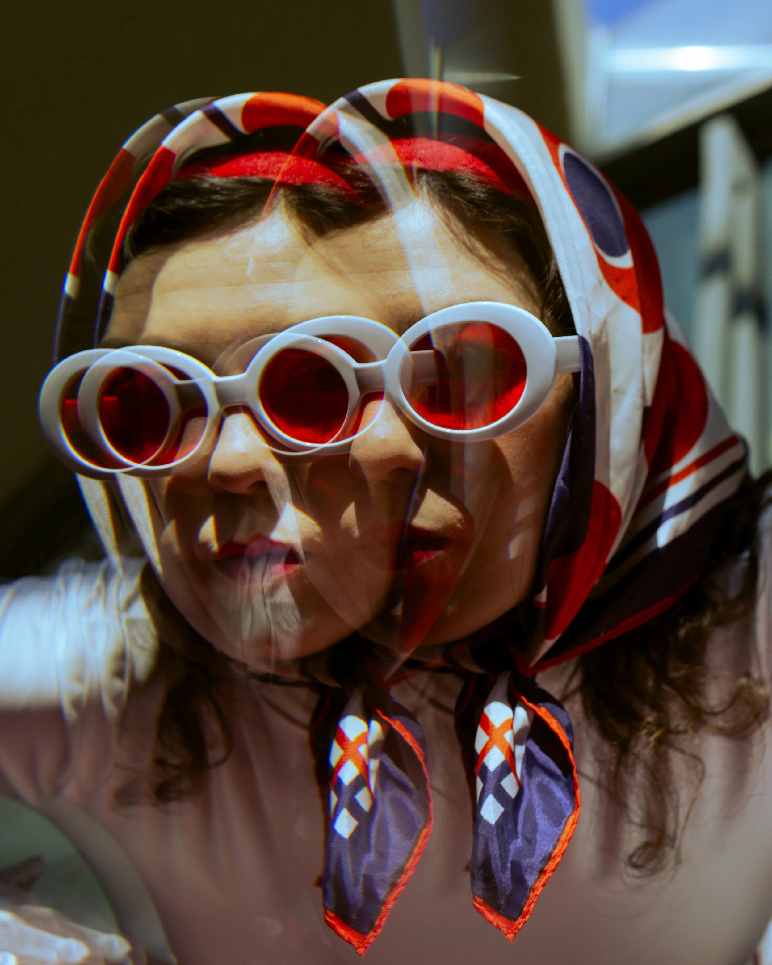 Close-up of a child's head with curly hair wearing colorful heart-shaped glasses and a red, white, and blue patterned headscarf.