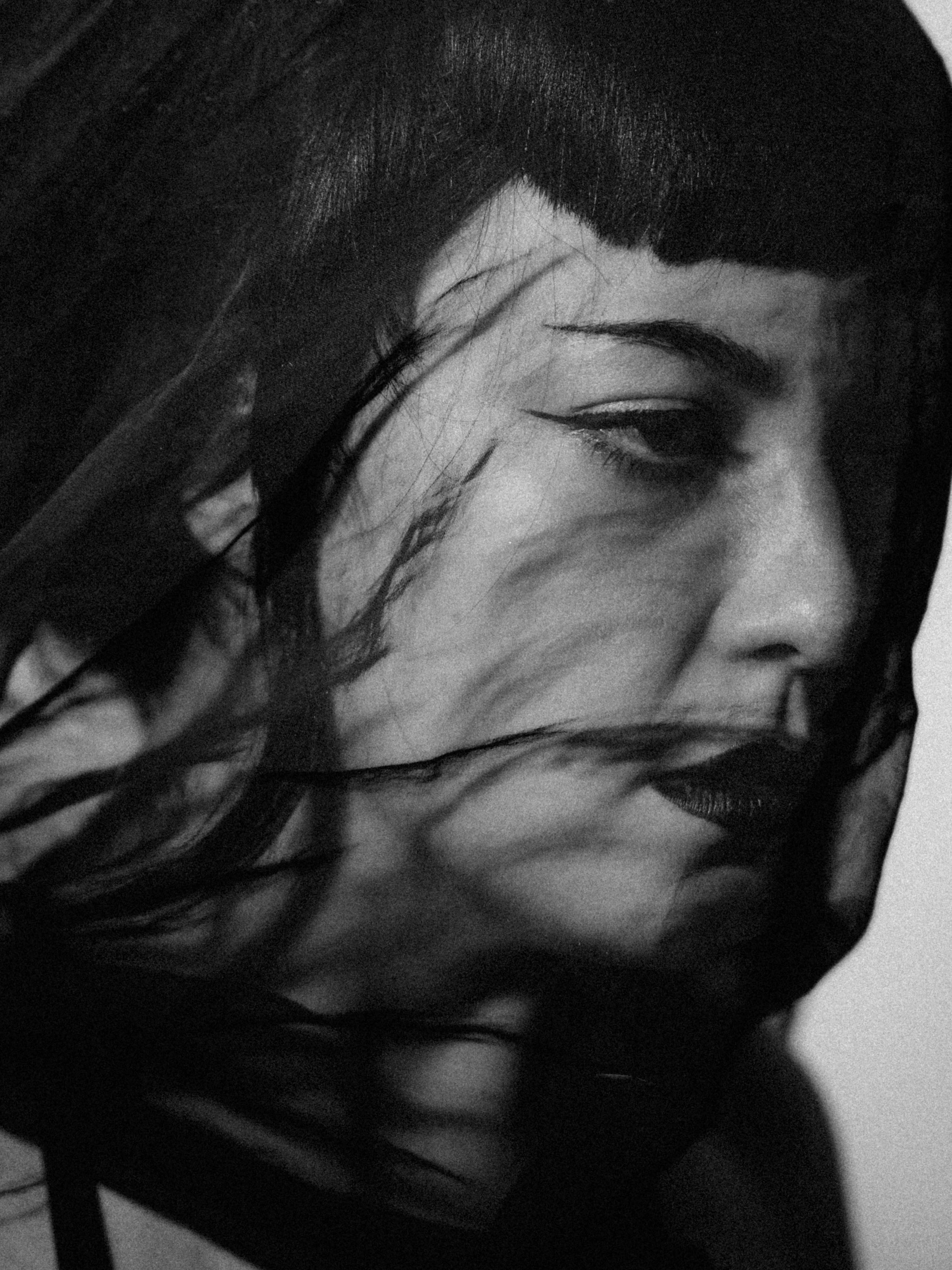 Close-up of a woman's face with dark hair and makeup, viewed partly and in black and white.