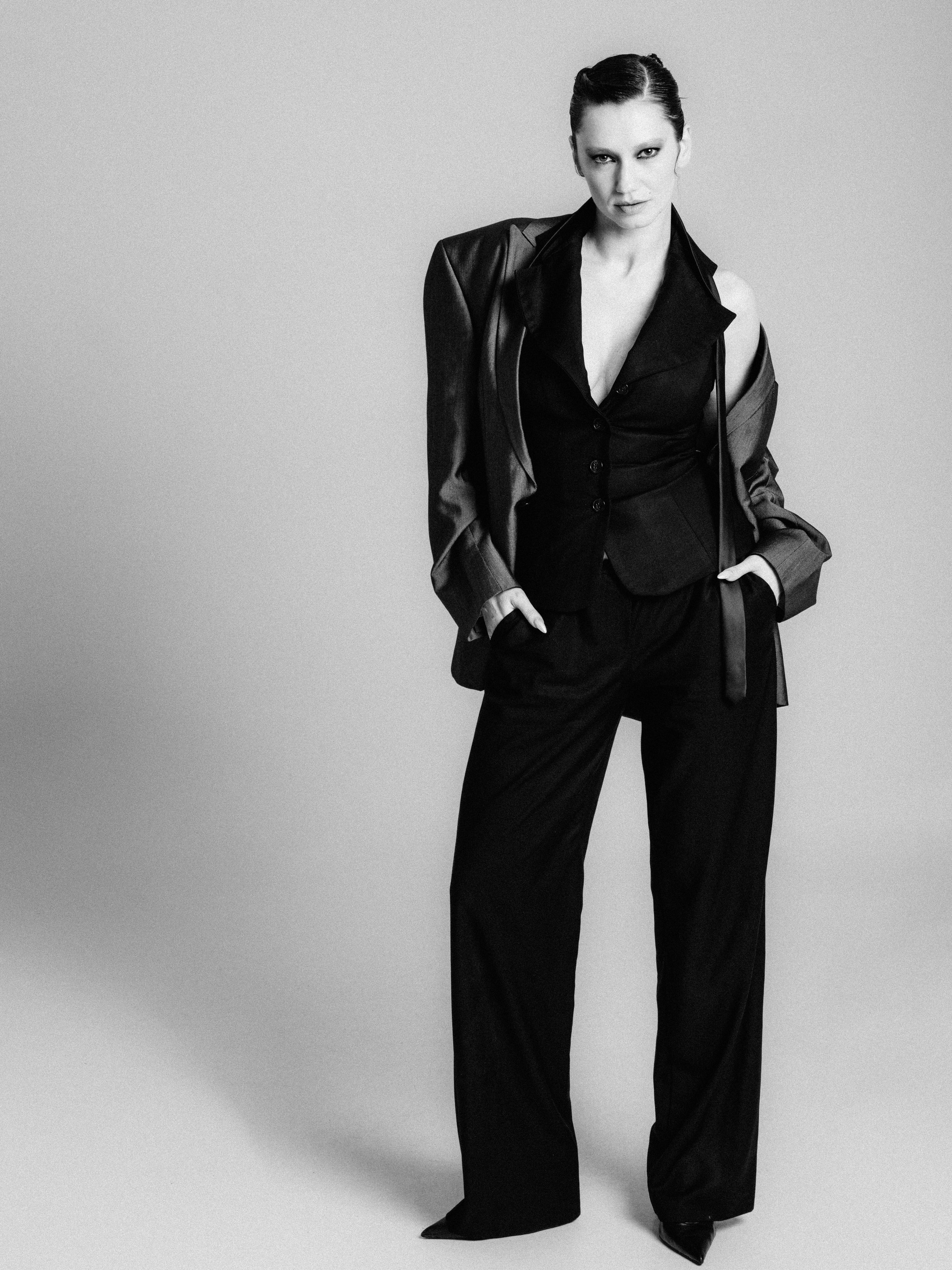 Black and white photo of a woman with short hair, wearing a suit with a jacket and high-waisted pants, standing against a plain background.