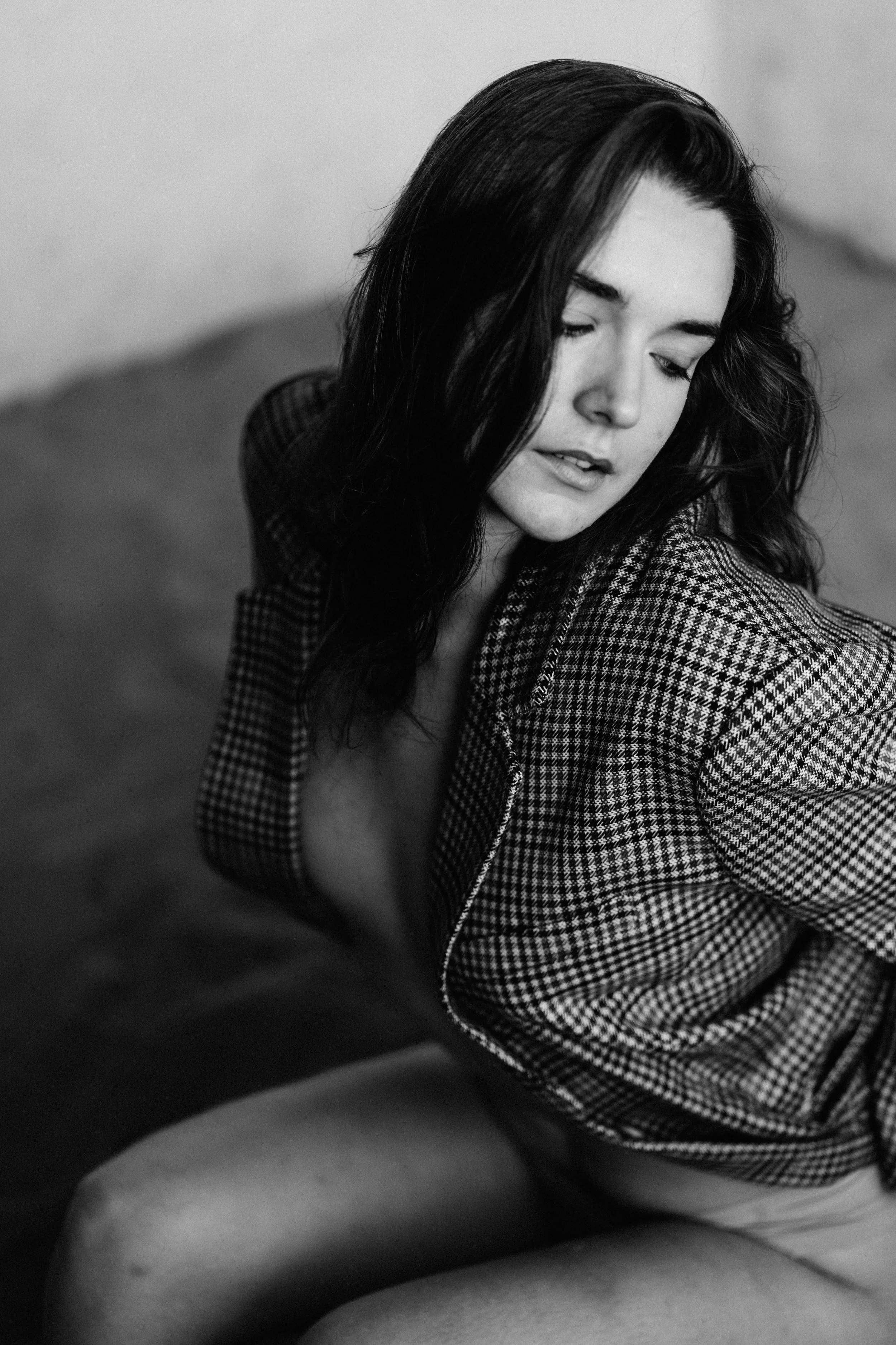 A woman with dark hair wearing a checkered jacket, looking downward, in a black-and-white photograph.