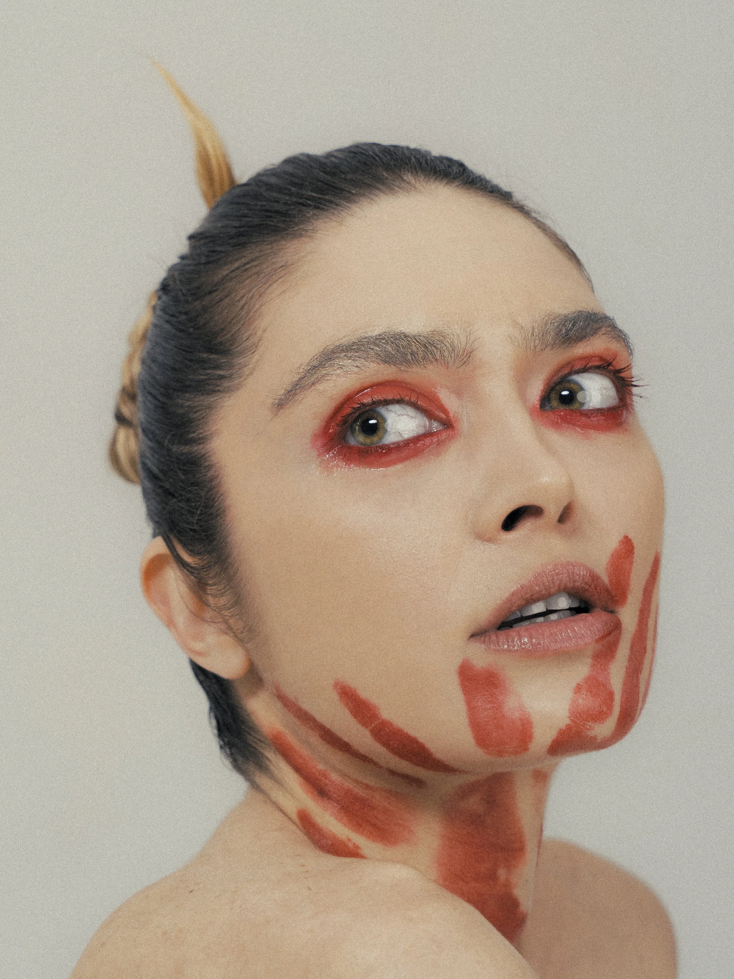 A close-up of a woman with artistic makeup and body paint resembling a giraffe, with her head slightly turned to the right, showing her face, neck, and shoulder against a plain background.
