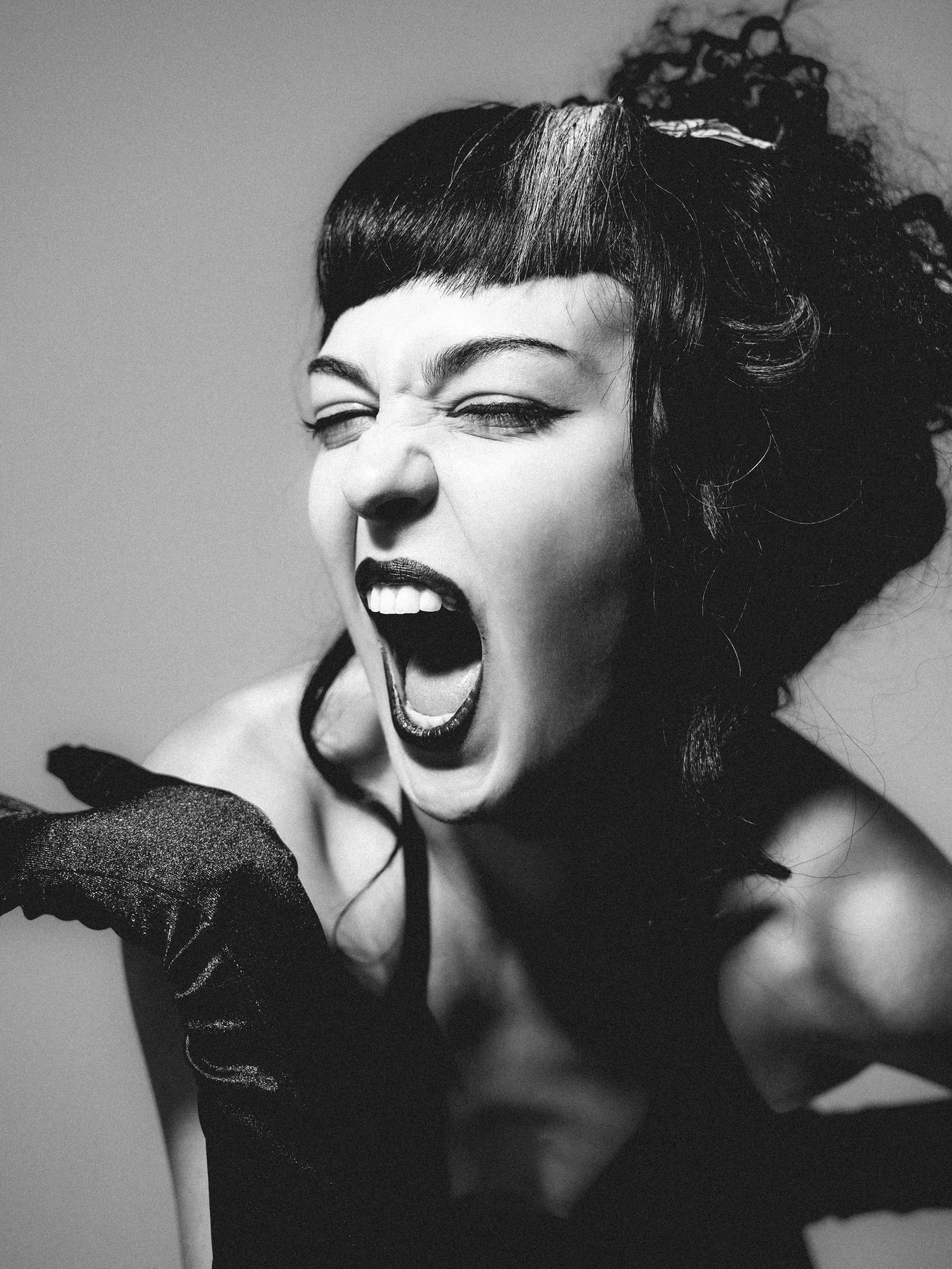 Black and white photo of a woman with short dark hair and bangs, showing her mid-yawn with eyes closed and mouth open.