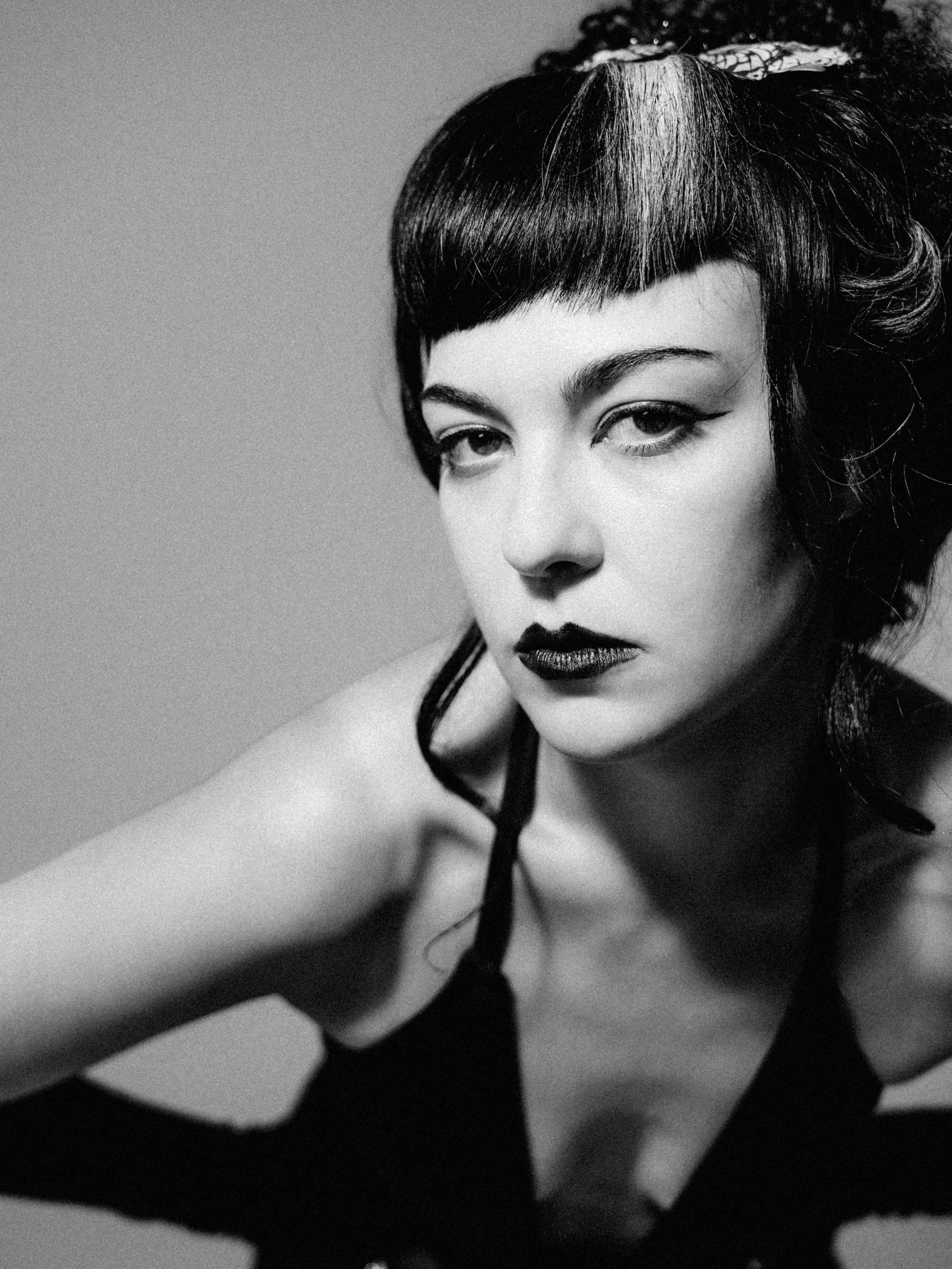 Black and white portrait of a woman with short, dark hair styled in a vintage fashion, bold makeup, and a confident expression.