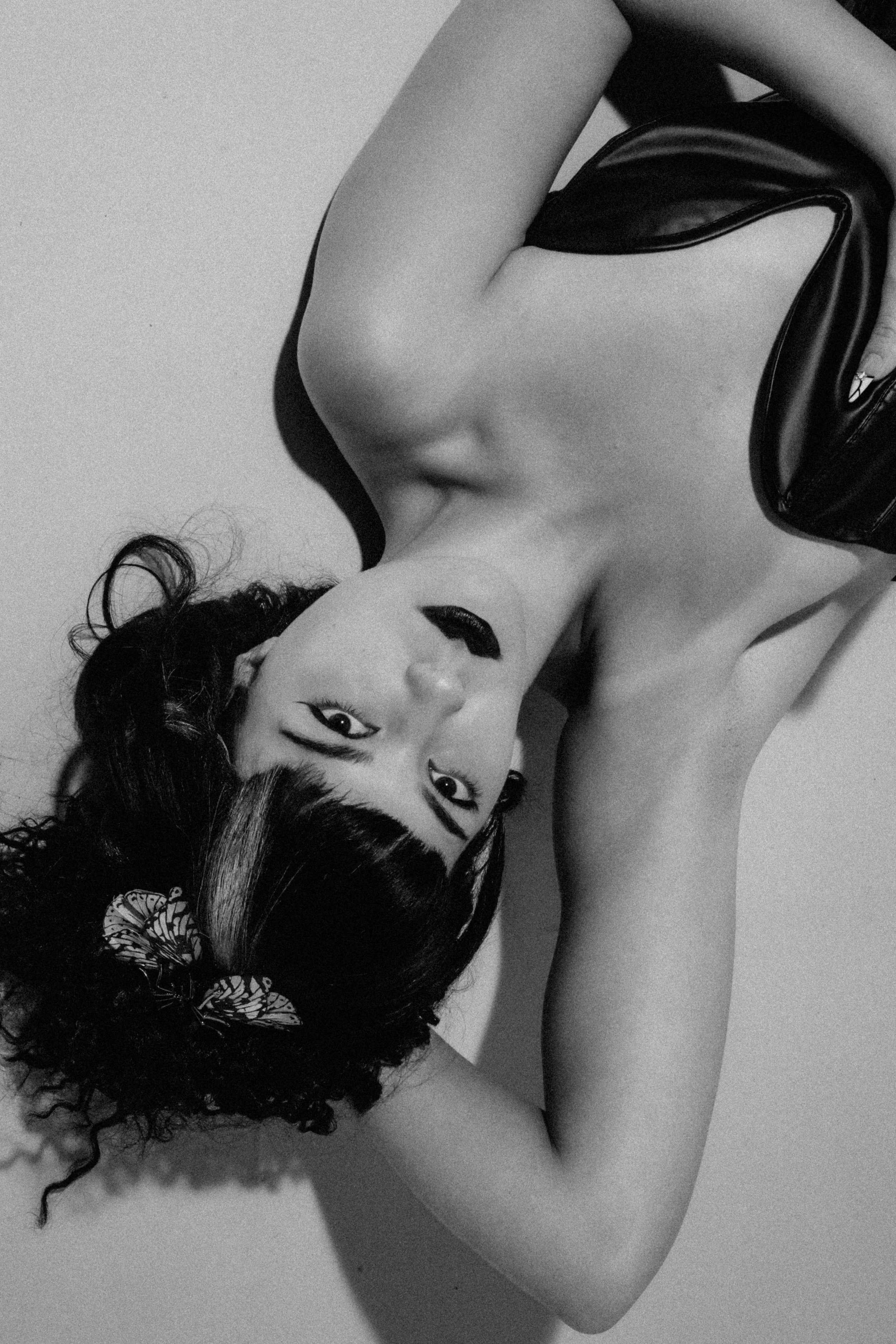 Black and white photograph of a woman with curly hair lying down, resting her head on her arm, with a butterfly hair clip in her hair.