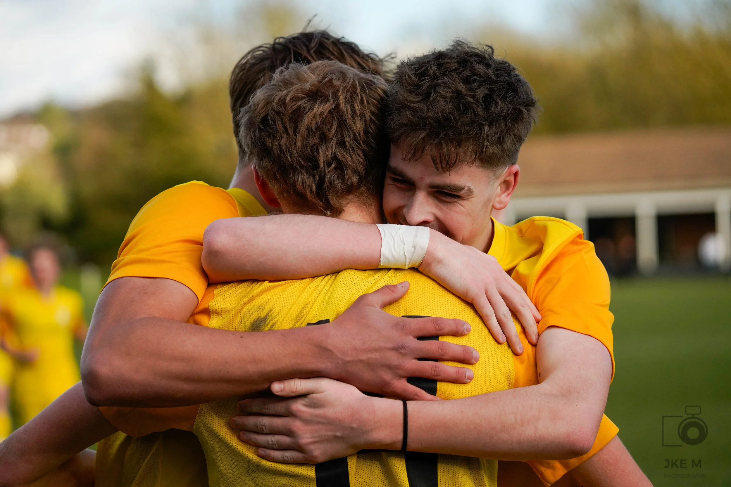 Two male football players in yellow kits are hugging each other in celebration.