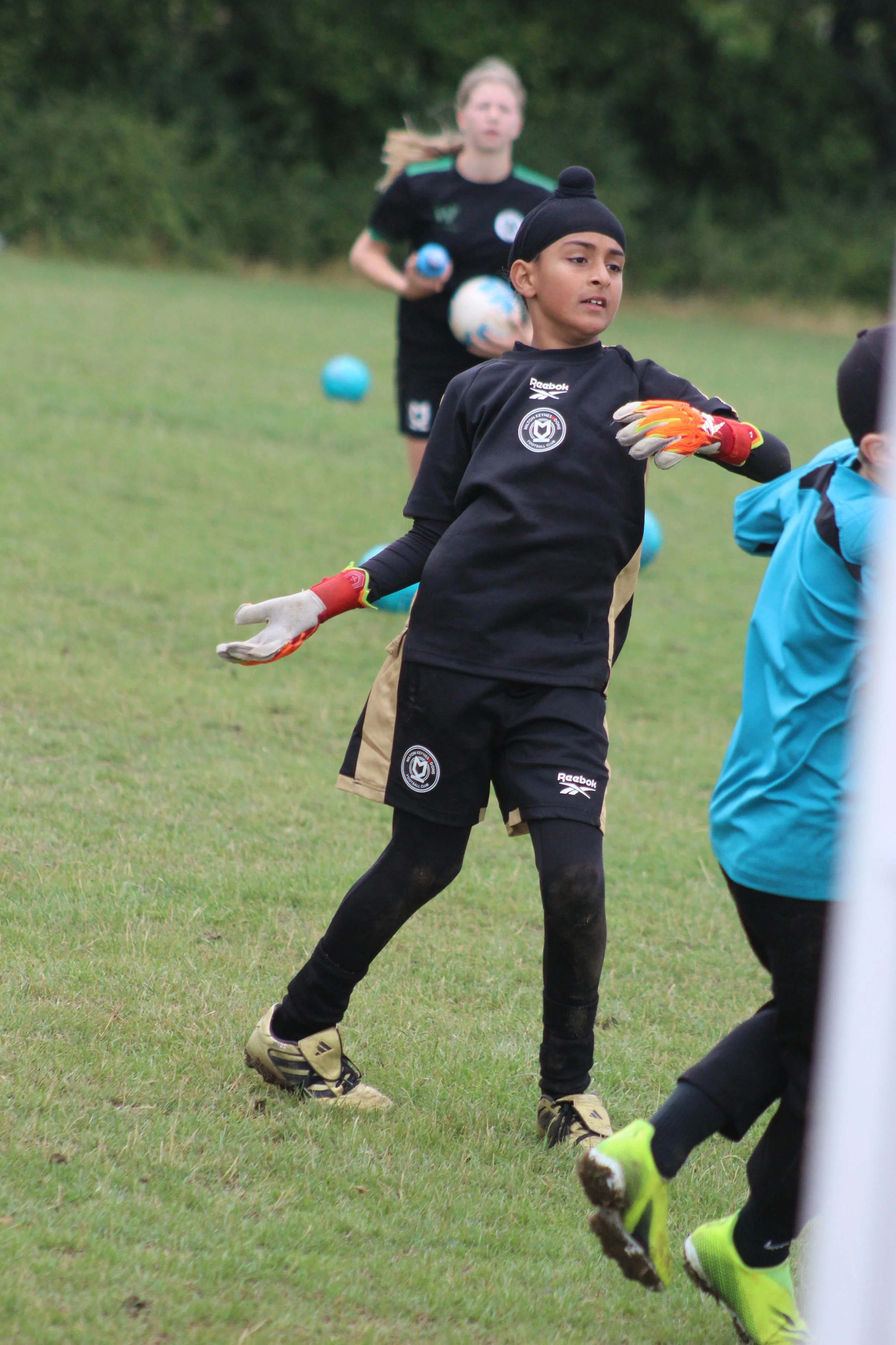 Young goalkeeper mid action, focus on a boy wearing a black Reebok Mk Training shirt with gloves.