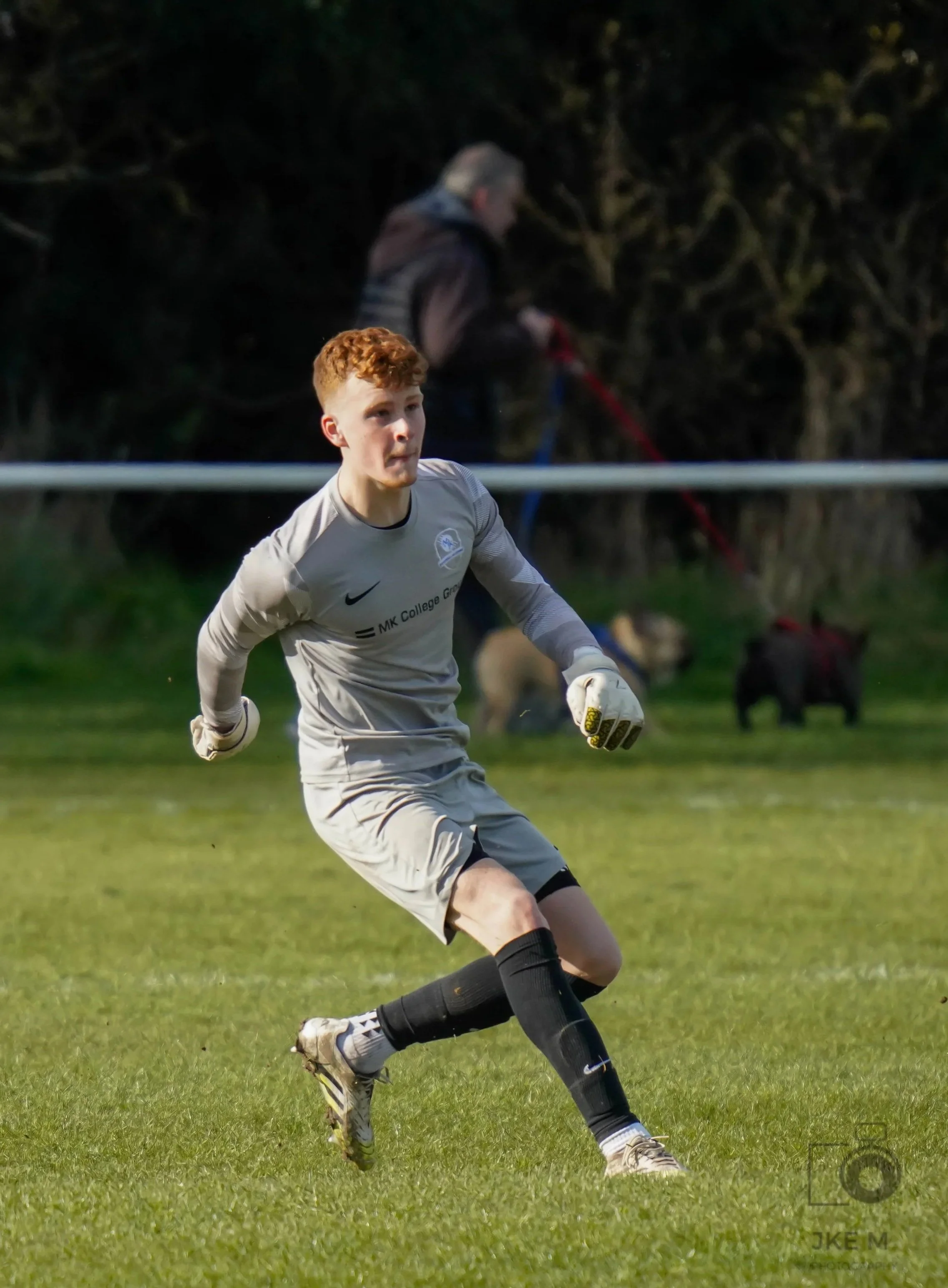 A young male soccer player with red hair and a prosthetic leg playing on a soccer field during daytime.
