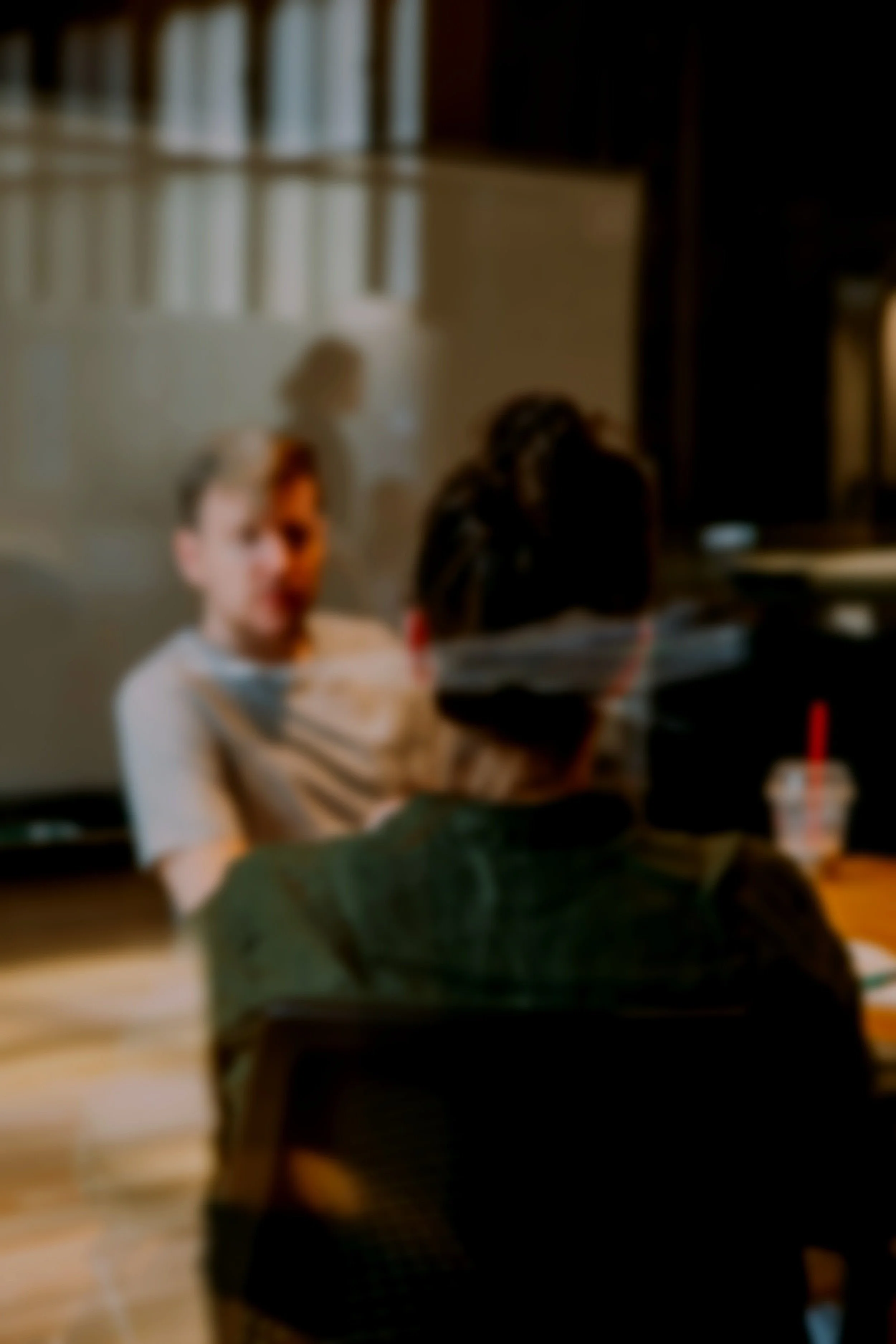 Two young boys sitting at a table in a restaurant, with one facing away and the other in a blurred background, and a cup with a red straw on the table.