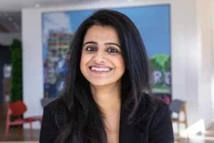 A woman with long dark hair smiling indoors with a colorful mural in the background.