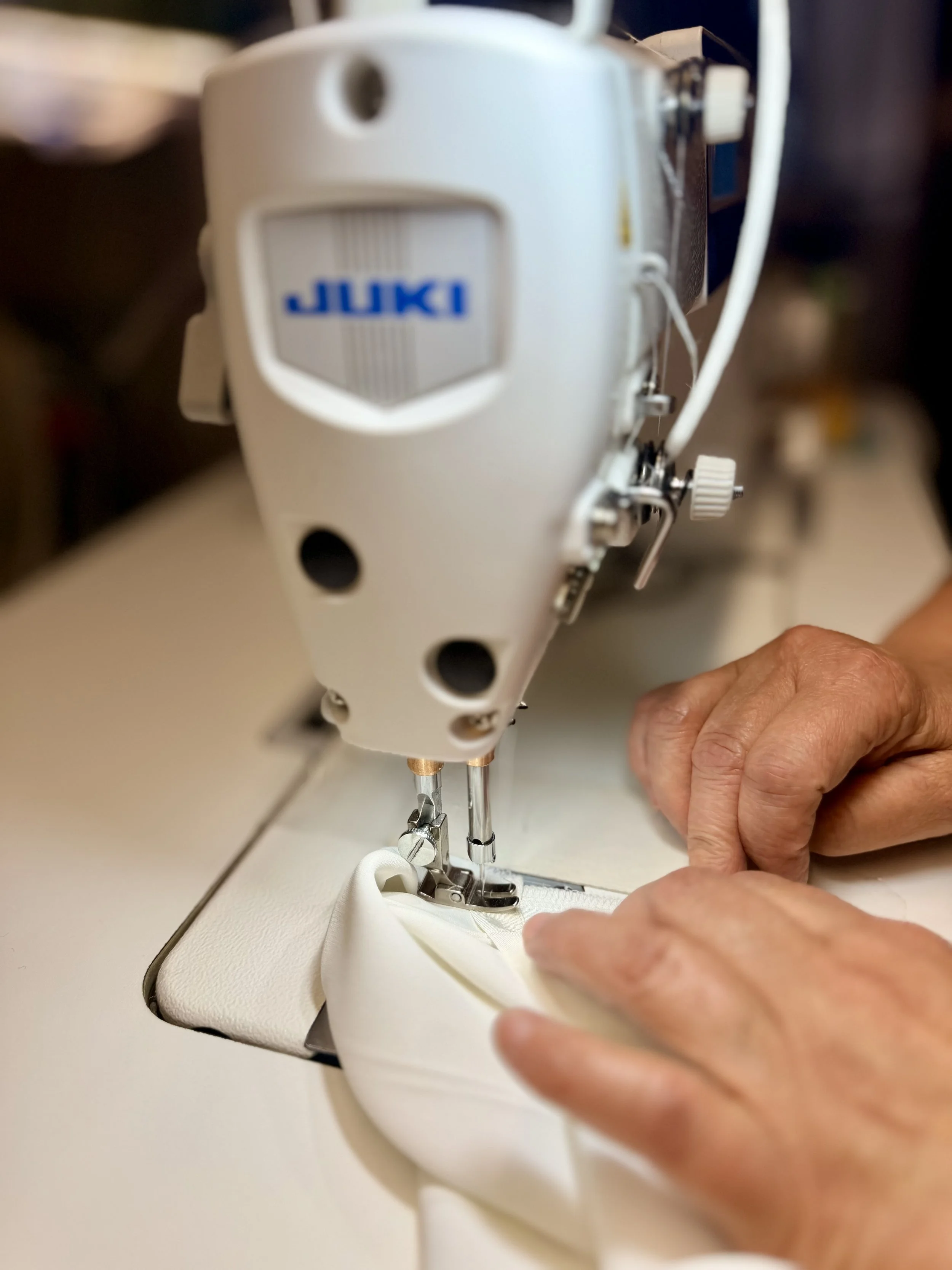 A person sewing on a Juki sewing machine with white fabric under the needle.