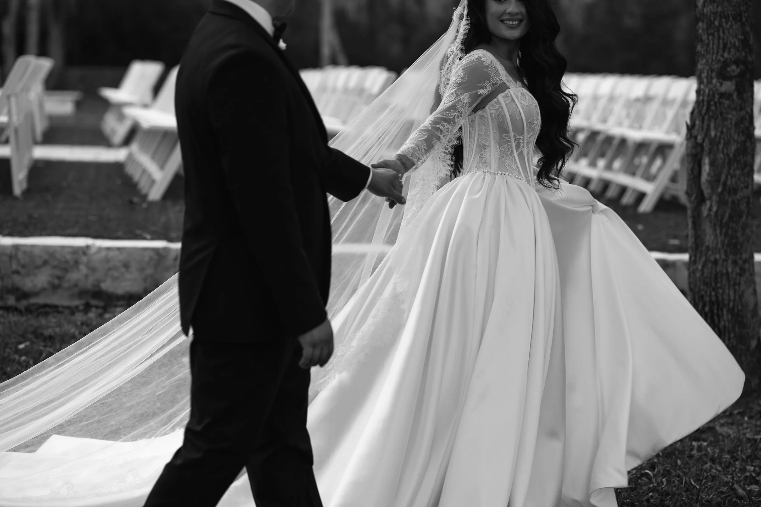A bride in a wedding dress holding hands with someone in a tuxedo during a wedding ceremony outdoors.