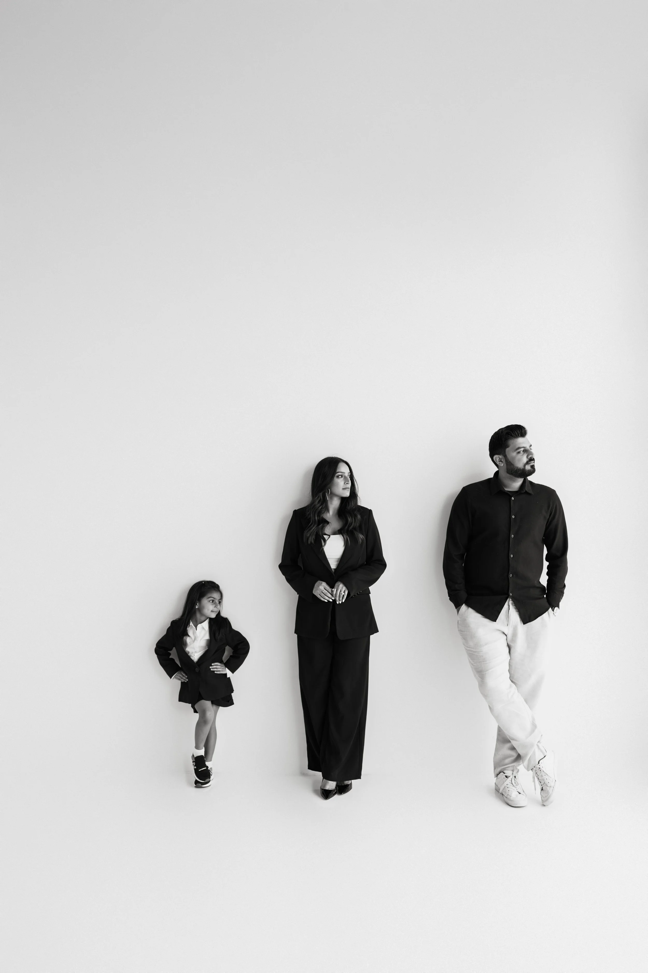 A black-and-white photo of an Asian woman, an Asian girl, and a man standing against a plain white wall. The woman and girl are looking to the left side, while the man gazes slightly upward and to the right. The woman and girl are dressed in formal b