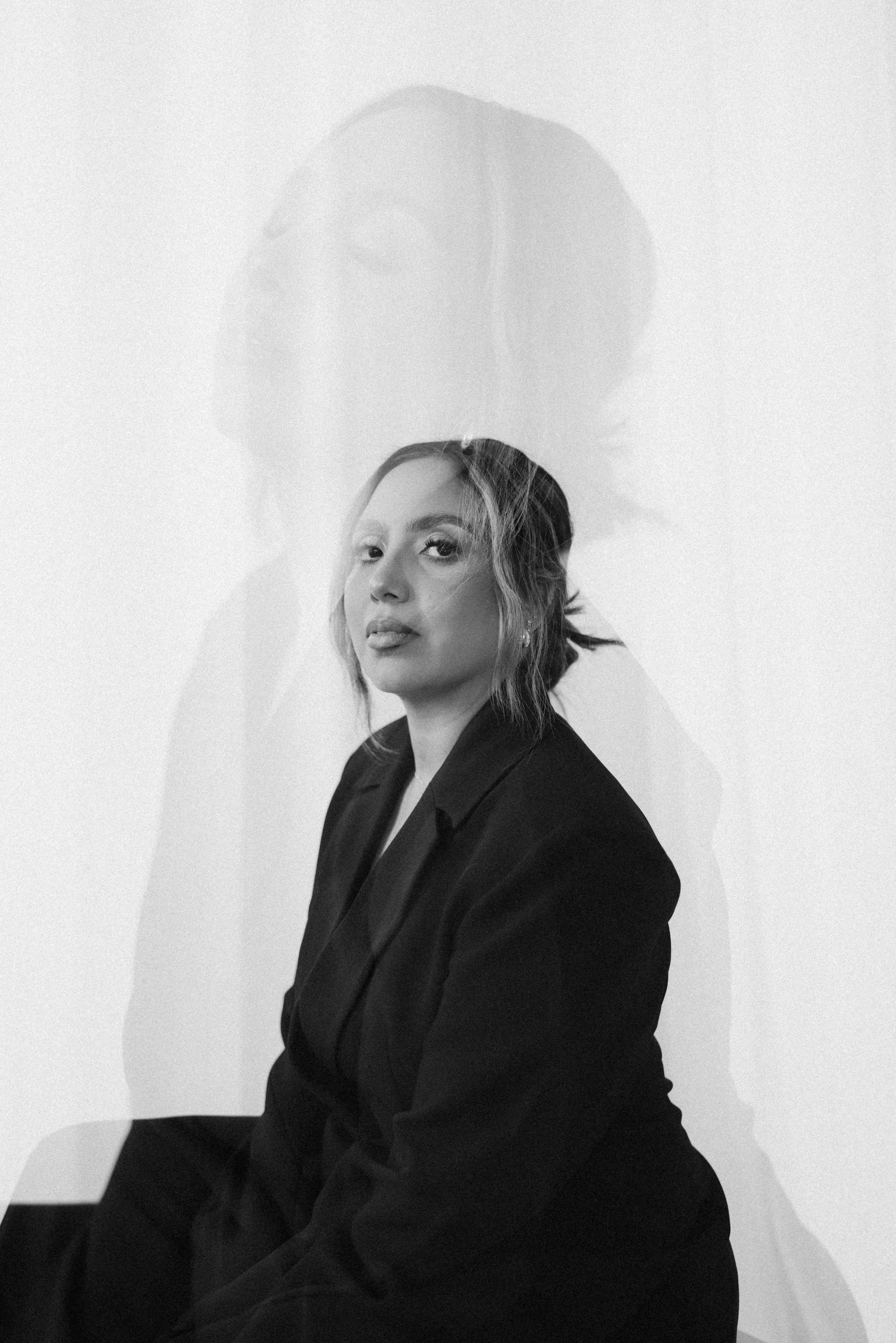 Black and white portrait of a woman with short hair, wearing a dark blazer, looking at the camera with a neutral expression, against a plain background.