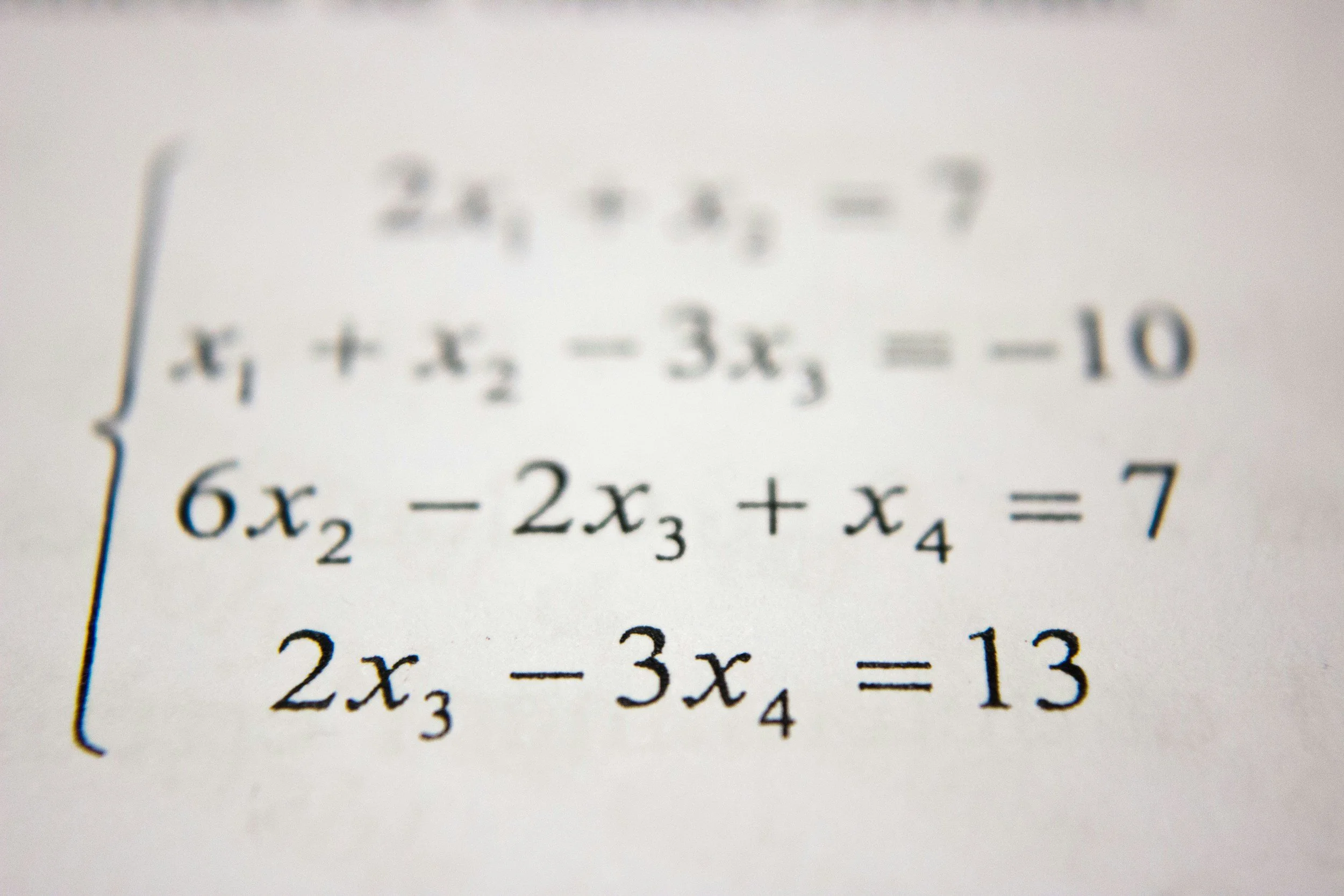 A printed system of linear equations on paper, showing three equations with variables x2, x3, x4.