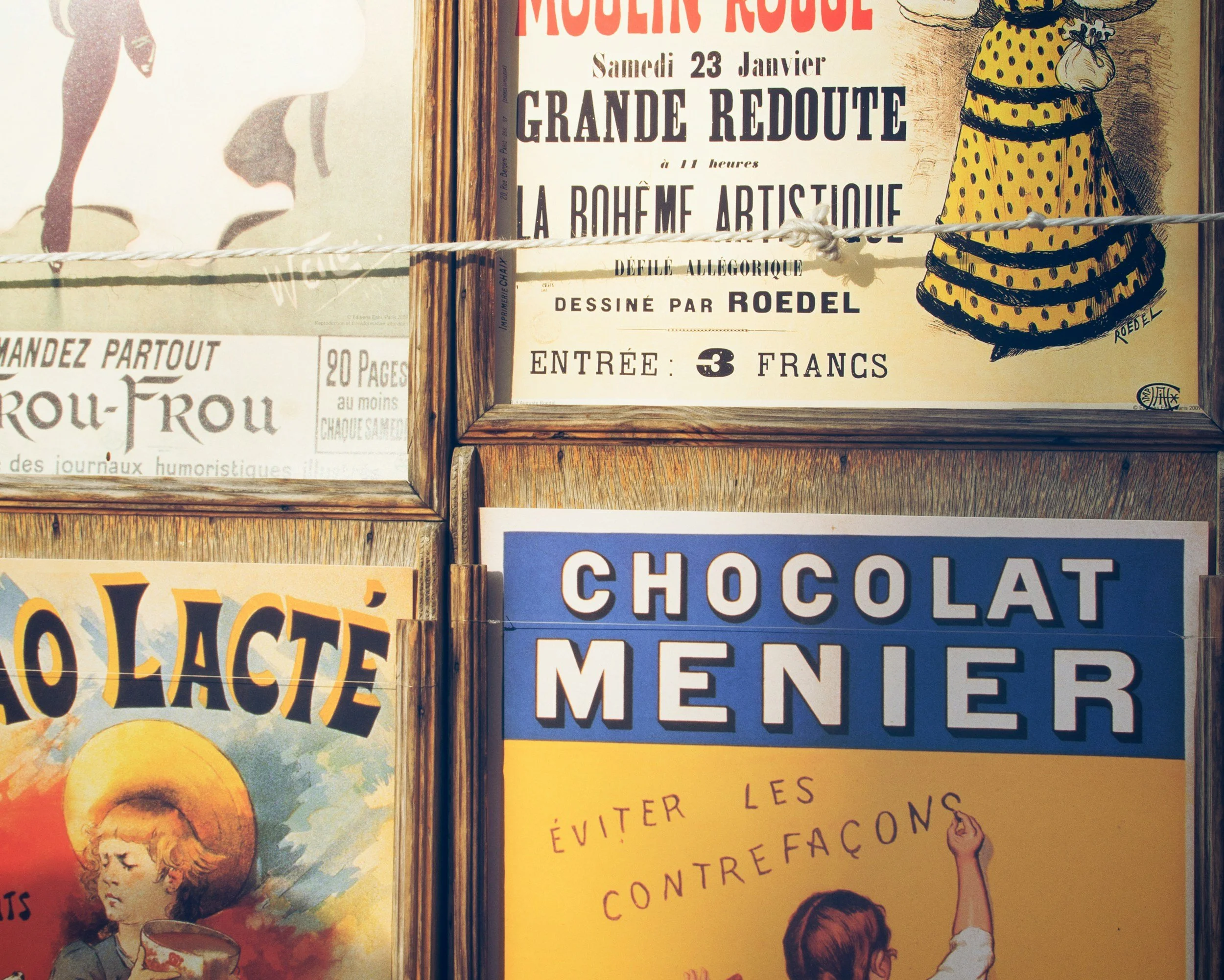 Display of vintage French posters and signs, including an advertisement for a concert and a chocolate brand, framed on a wooden wall.