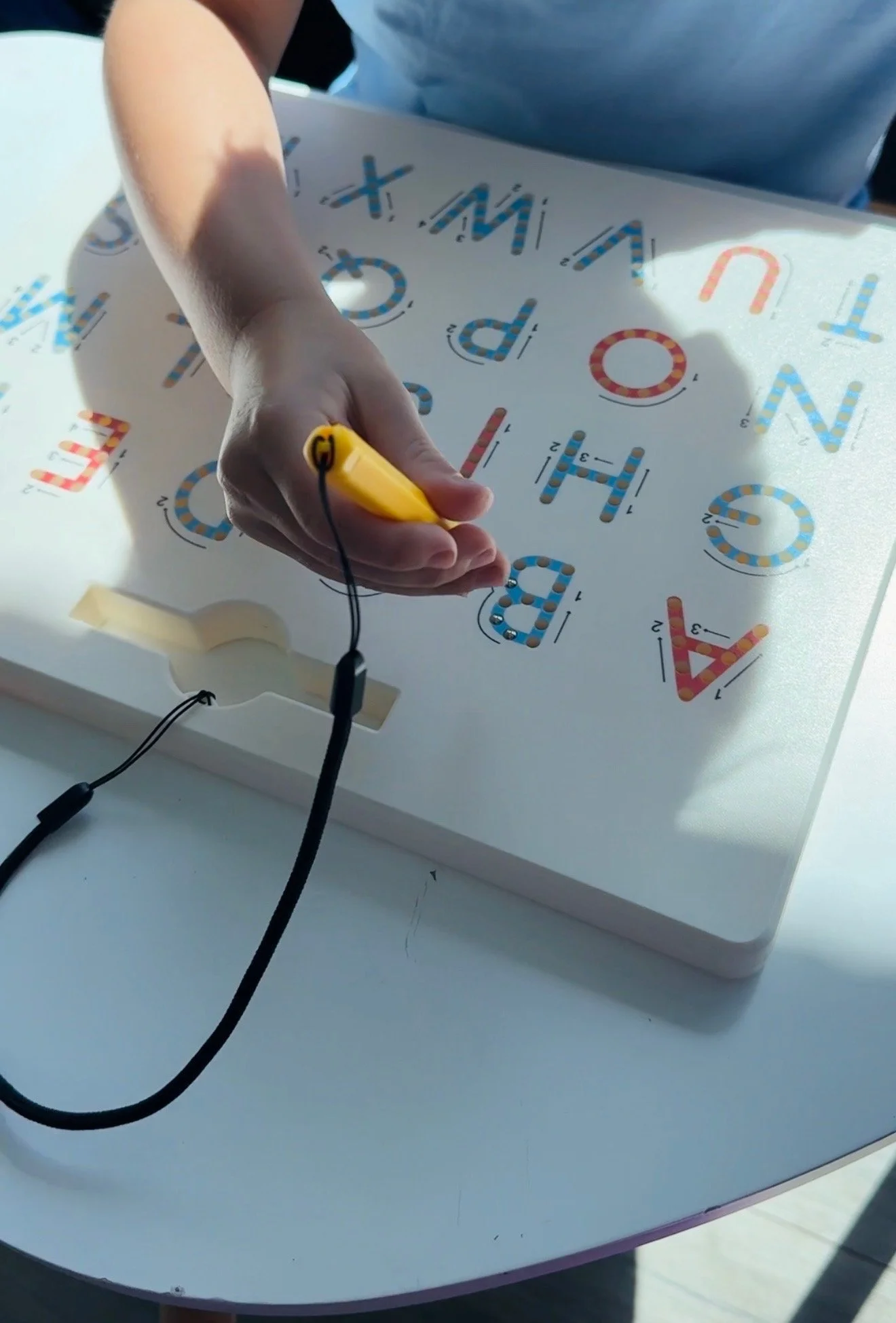 A person is using a handheld device to trace a letter on a light-up educational board that displays colorful letters of the alphabet.