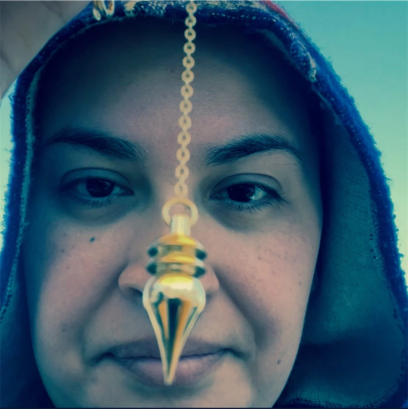 A woman with a black hoodie and a gold forehead chain with a pointed pendant covering her nose and upper lip.