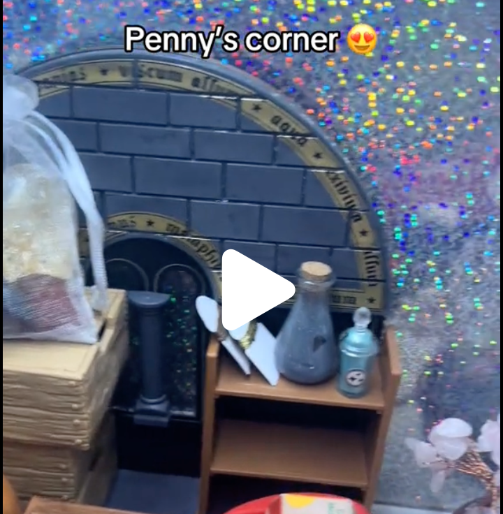 A decorated corner labeled "Penny's corner" with a glittery, multicolored backdrop, a mirror with a gold frame, a wooden shelf with a vintage glass bottle, a spray can, and some paper or books, reflecting a cozy, personalized space.