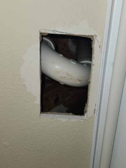 A hole in the drywall wall showing a white pipe inside. plumbing fix, plumber