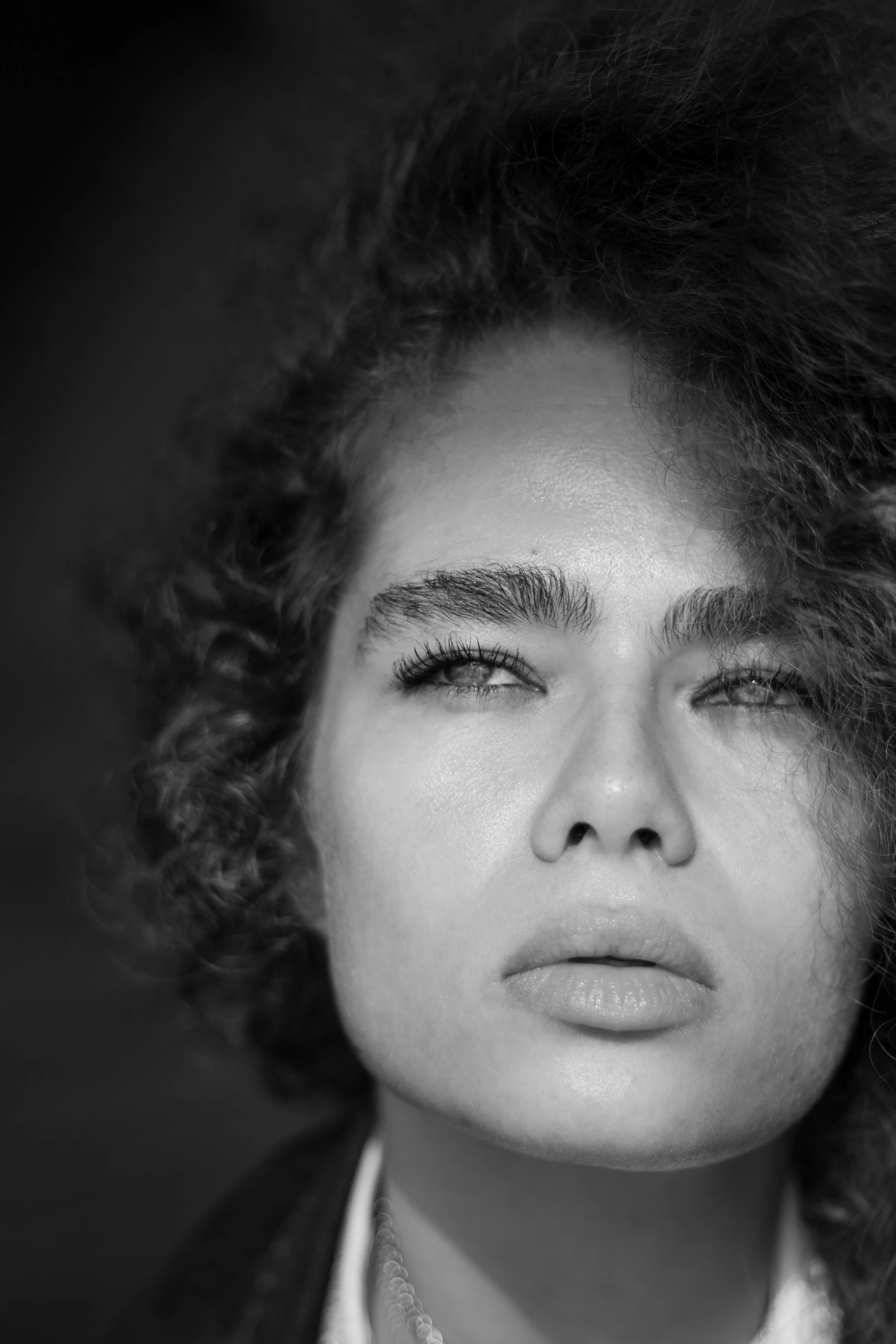 Portrait en noir et blanc d'une femme avec des cheveux bouclés, regardant légèrement vers le haut.
