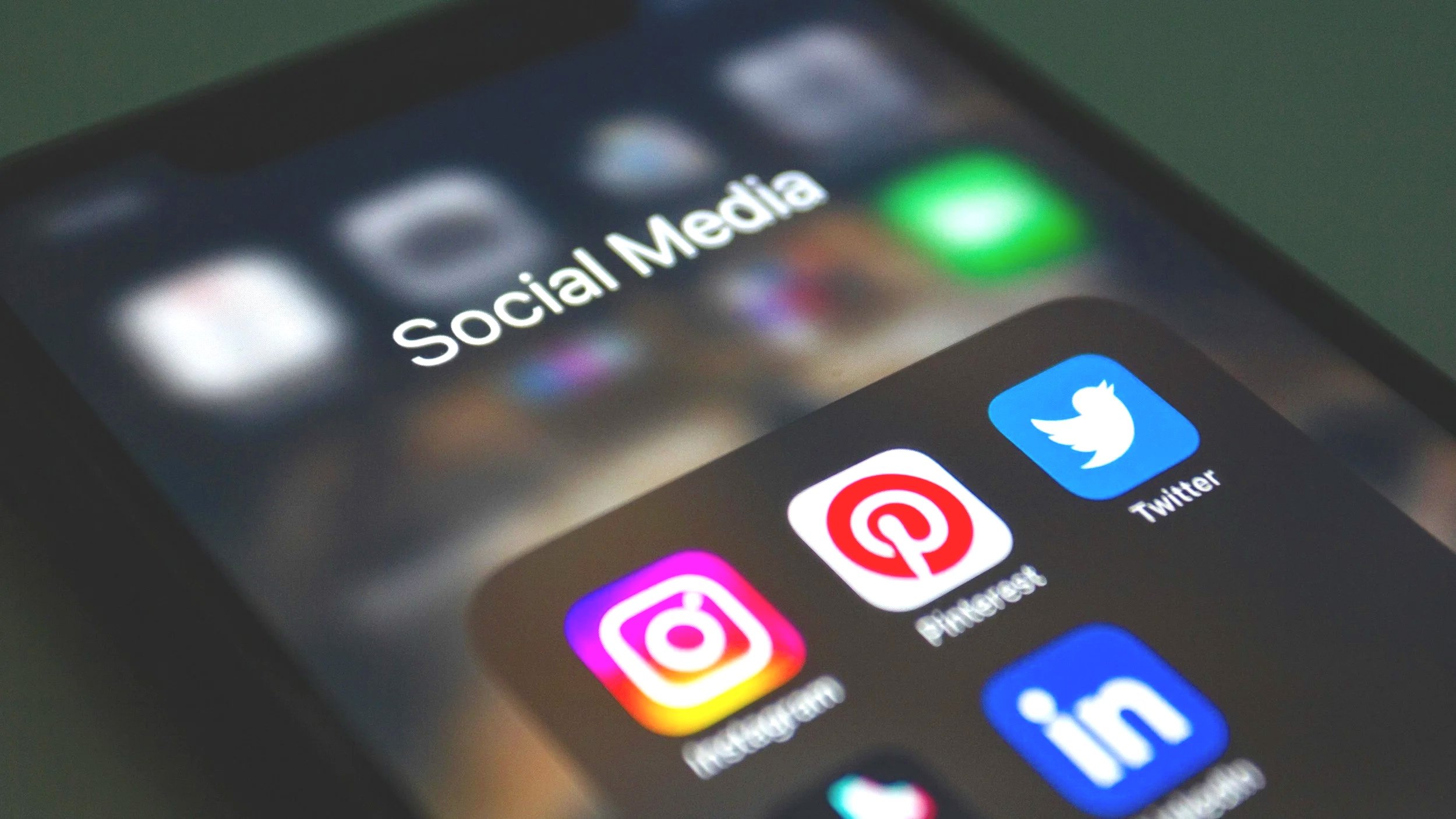 Close-up of a smartphone screen showing social media app icons, including Instagram, Pinterest, Twitter, and LinkedIn, with the folder labeled 'Social Media' at the top.