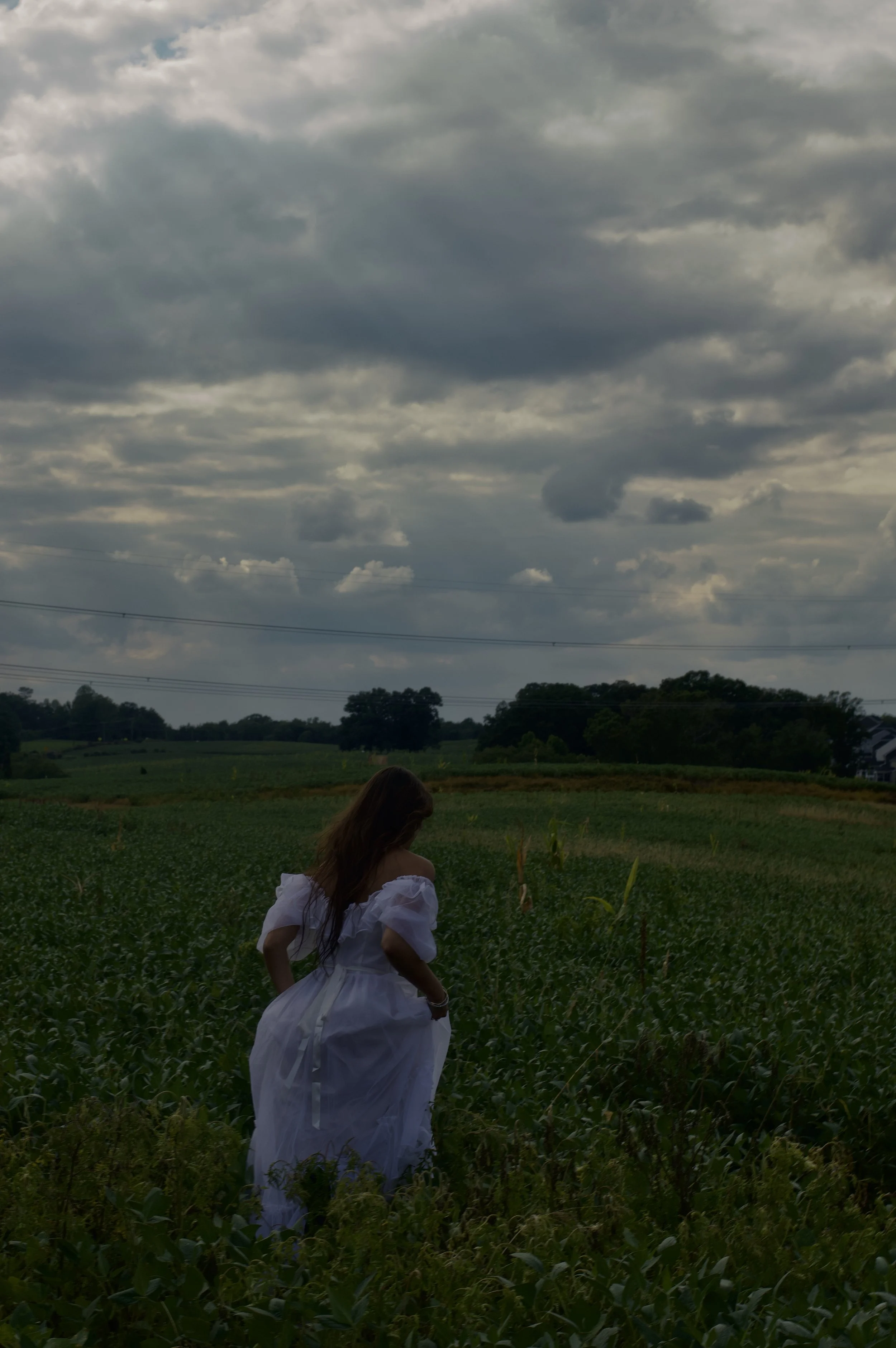 A woman in a white dress standing in a field under a cloudy sky.