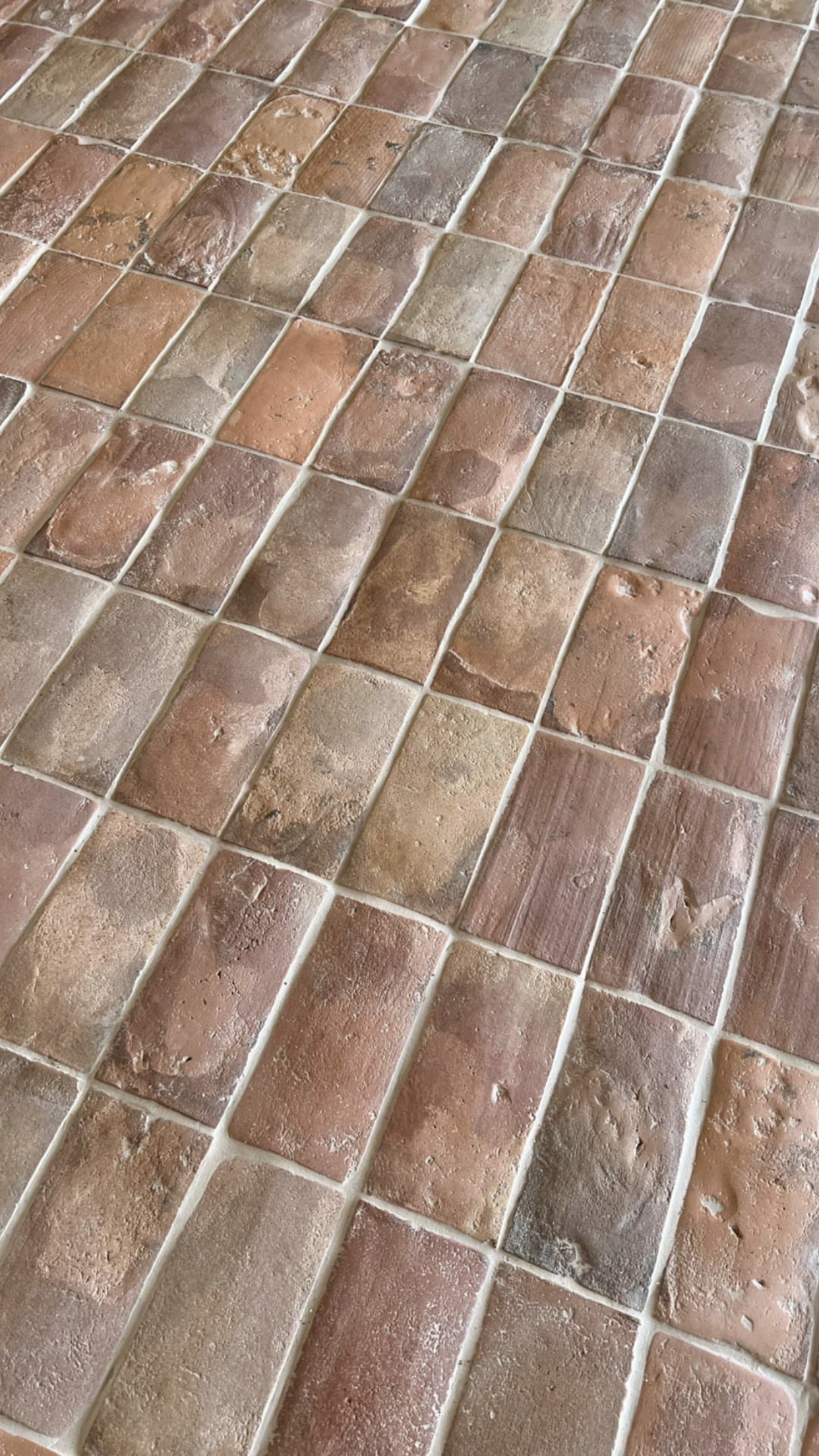Close-up of a tiled floor with irregularly shaped, reddish-brown tiles and light-colored grout.