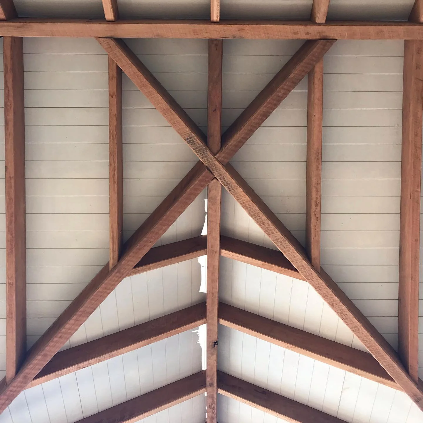 Wooden ceiling beams forming a triangular truss with a white ceiling panel between the beams.