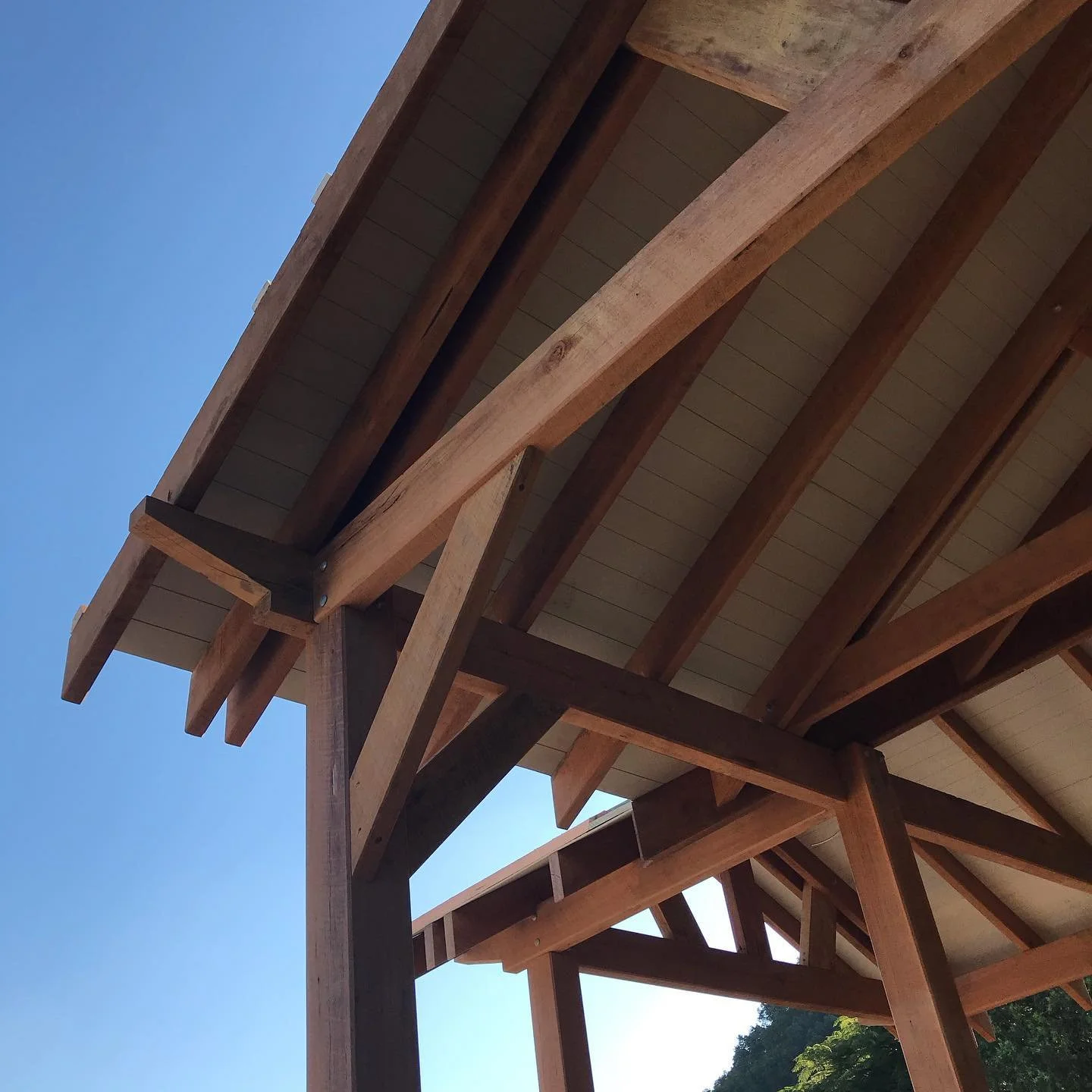 Close-up view of a wooden structure with beams and roofing, against a clear blue sky.