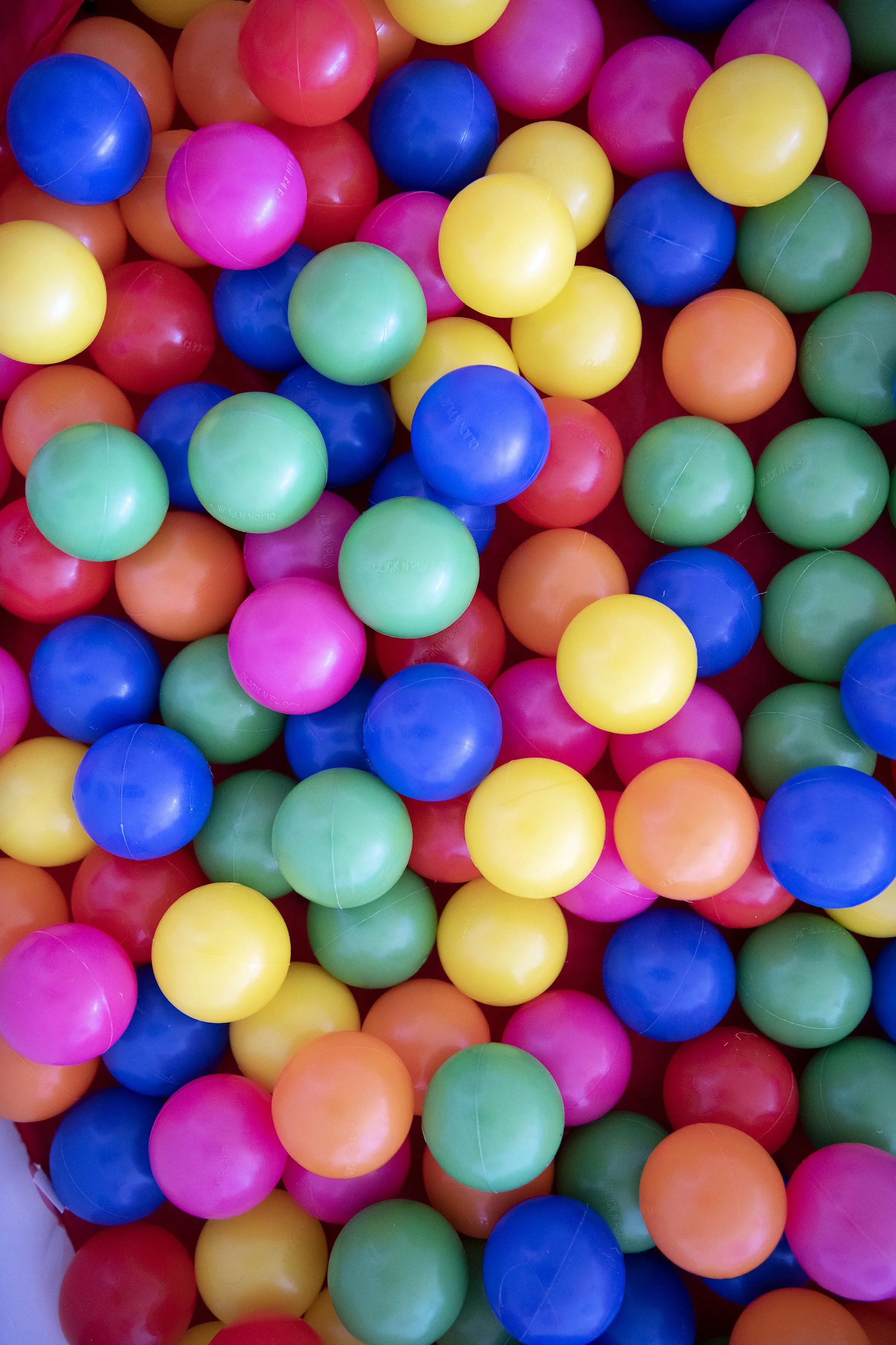 Colorful plastic balls in pink, blue, green, yellow, and orange filling a container.