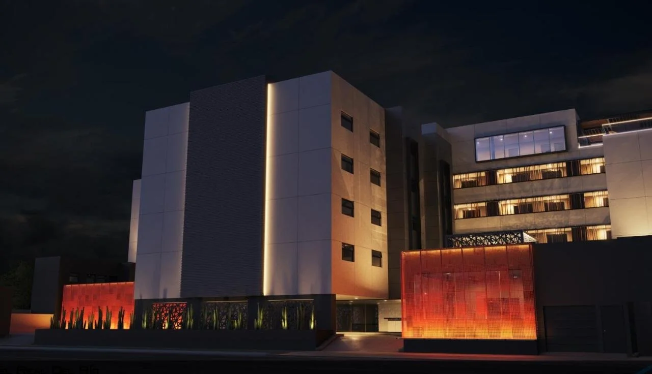 Night view of a modern multi-story building with illuminated windows and exterior lighting, featuring contemporary architectural design with clean lines and geometric shapes.