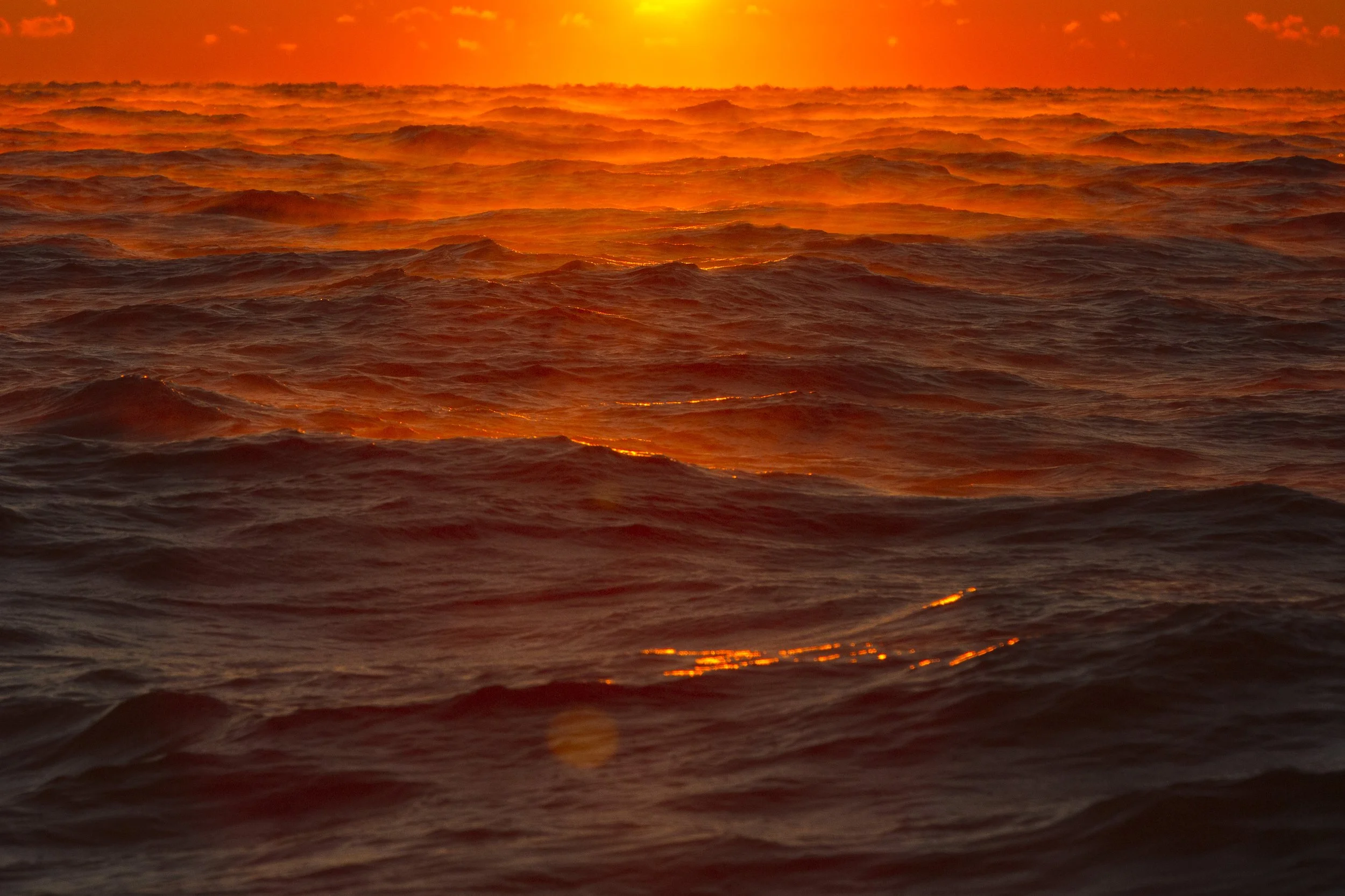 Ocean waves during sunset, with an orange and yellow sky reflecting on the water.