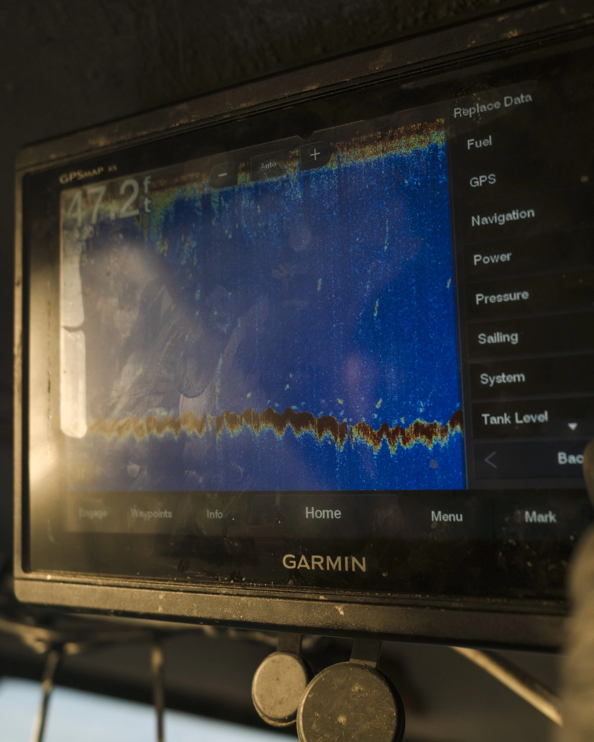 Garmin fishfinder display showing underwater sonar readings with water depth 47.2 feet, sonar signal data, and a menu with options like data, fuel, GPS, navigation, power, pressure, sailing, system, and tank level.