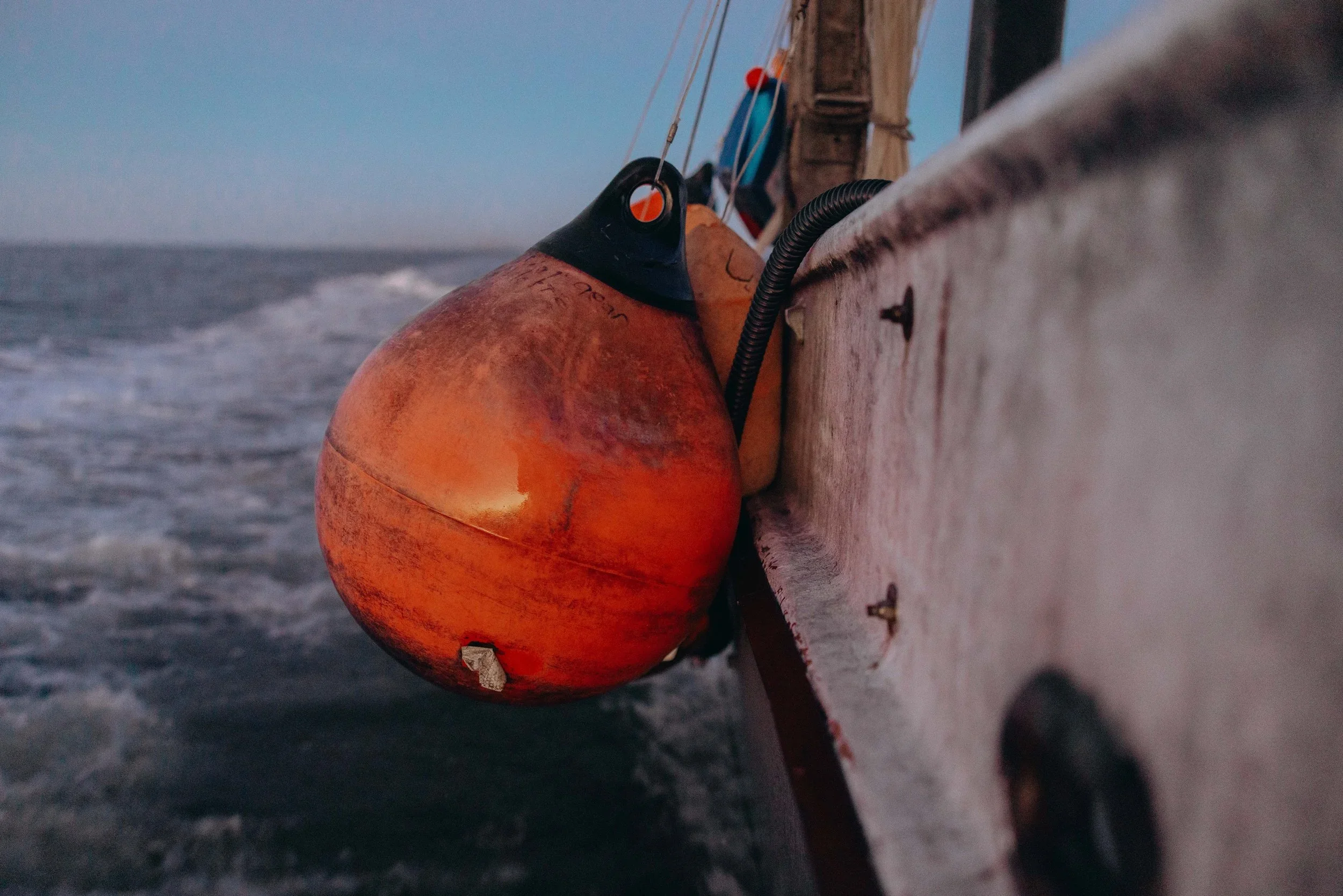 Close-up of an orange buoy attached to the side of a boat with a black top, floating on the water during sunset or dusk.
