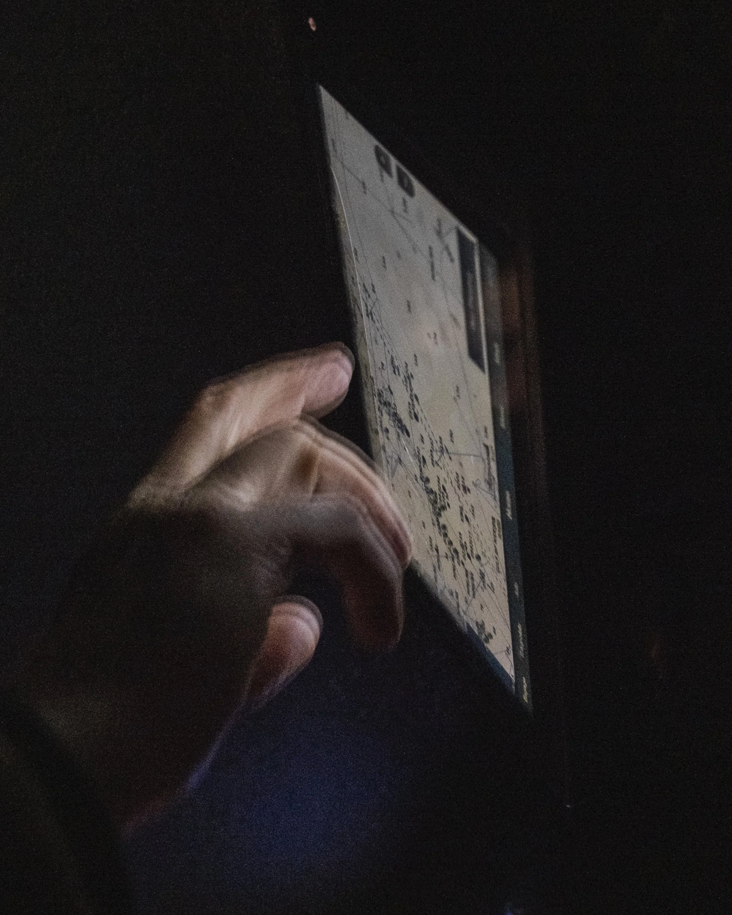A person holding a smartphone in a dark environment, with the phone's screen displaying a calendar or scheduling app