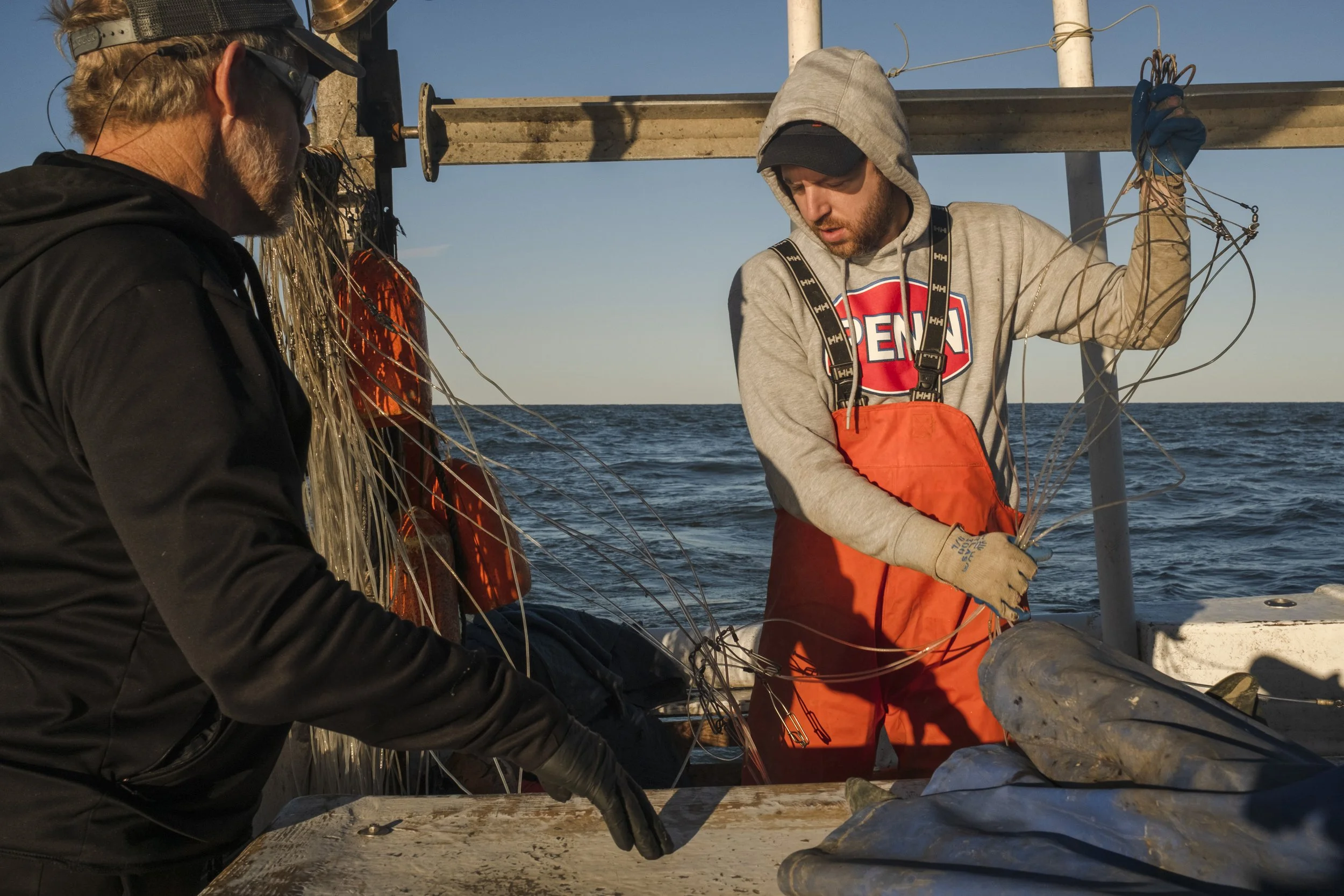 Two fishermen handling a large fish, likely a halibut or flatfish, on a boat in the open sea during daylight.