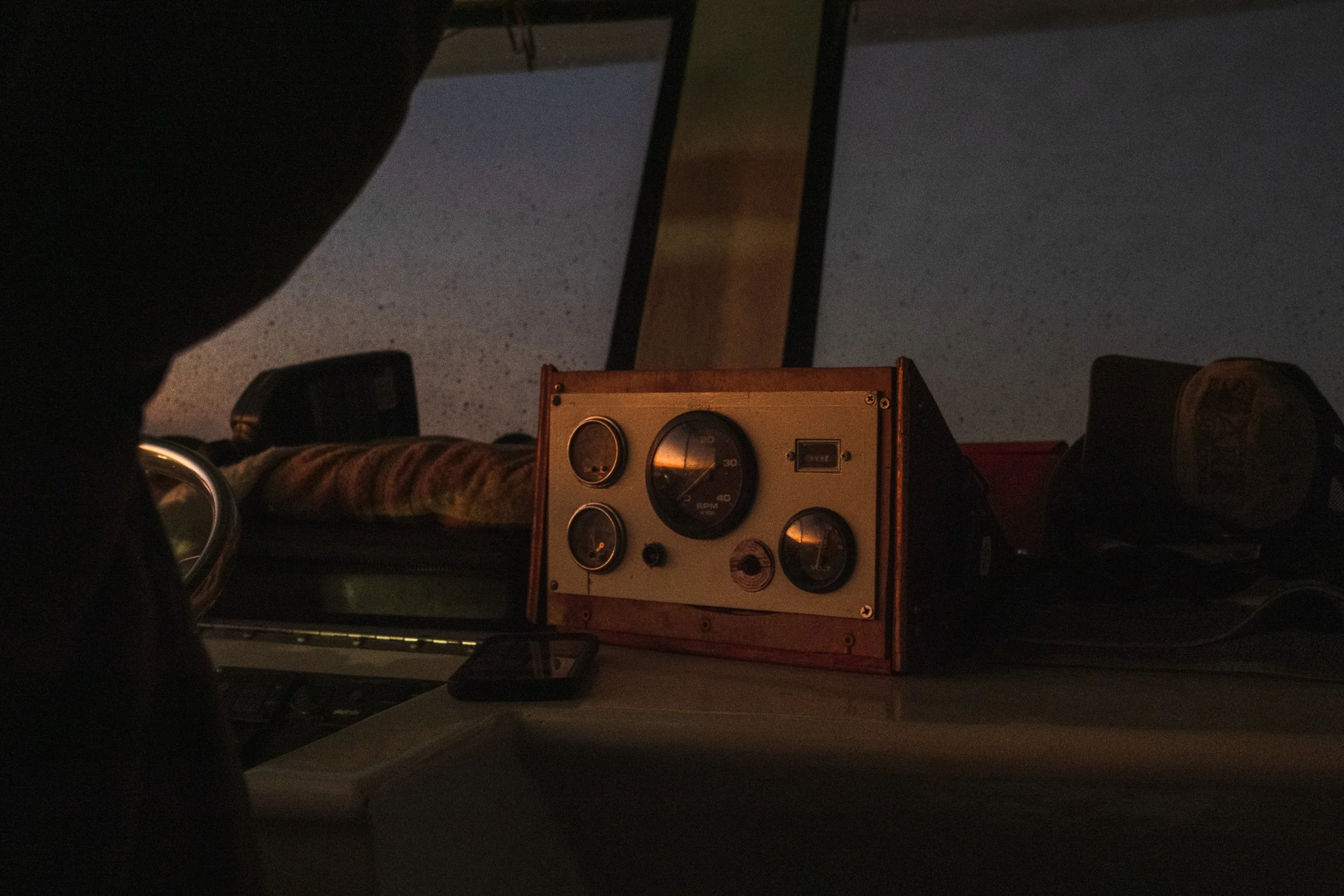 A dashboard with gauges, a timer, and a phone on a surface, with a dark sky outside.