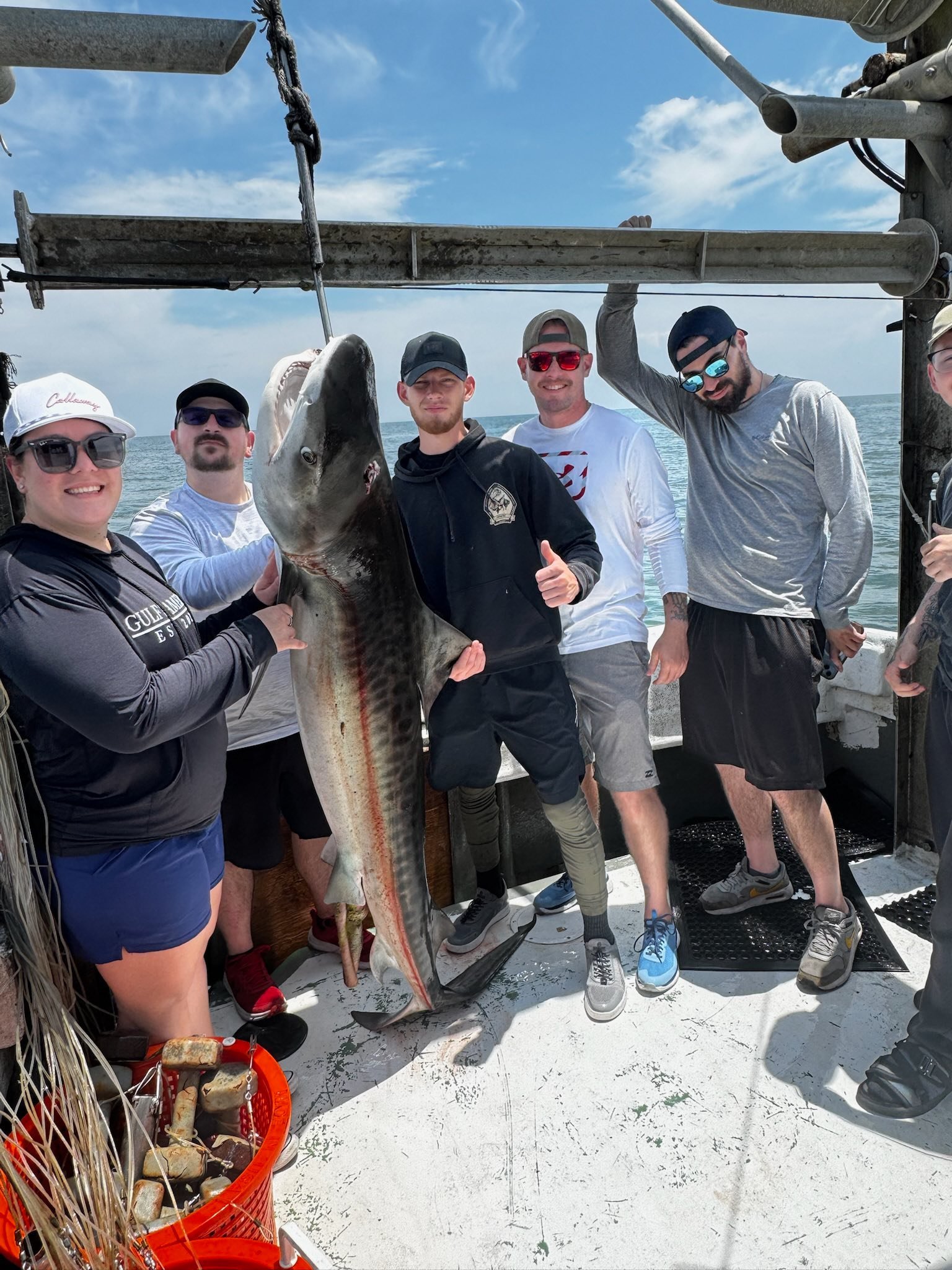 A group of people on a boat holding a large fish they caught, with a blue sky and ocean in the background.