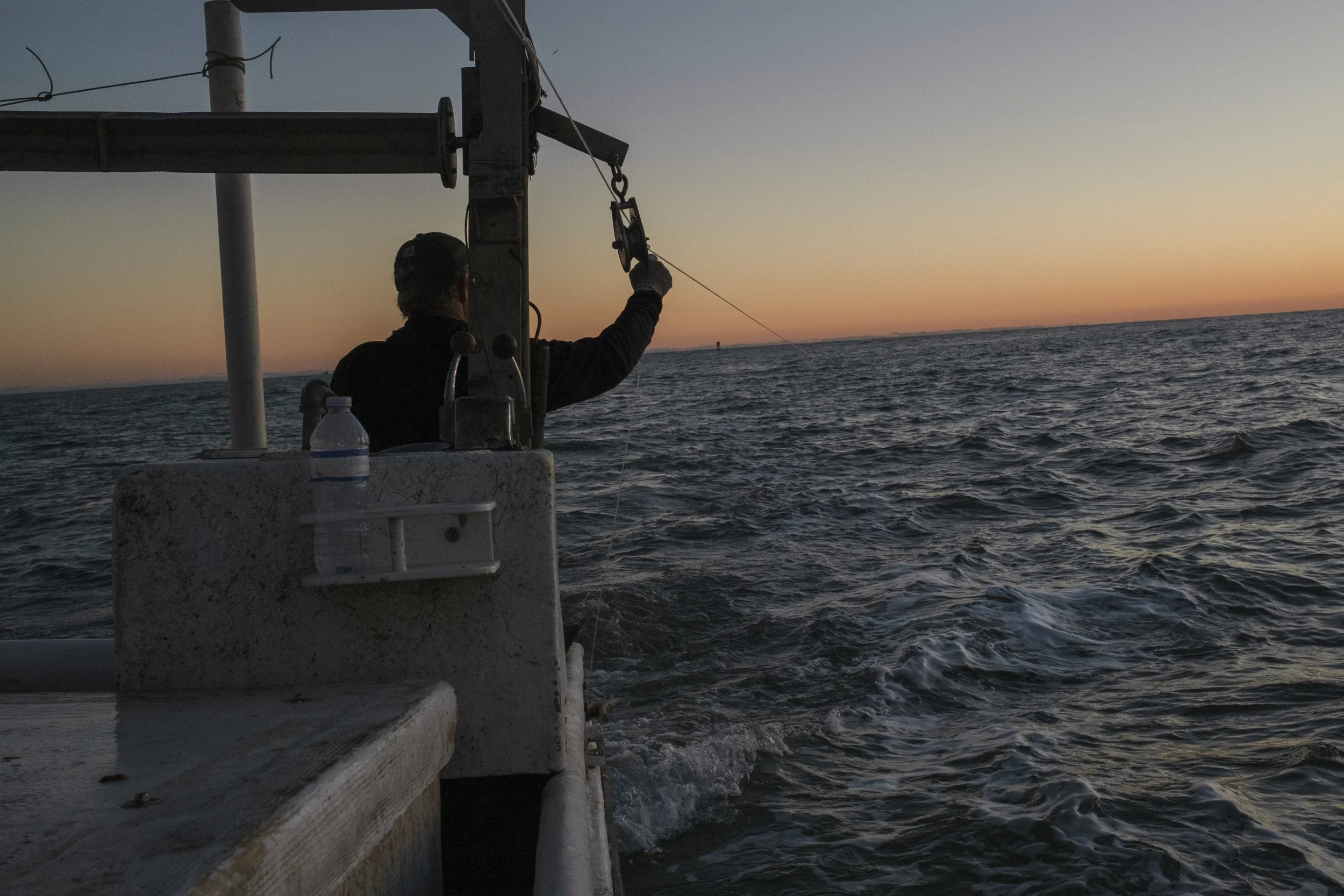 Person fishing on a boat during sunset in the ocean.