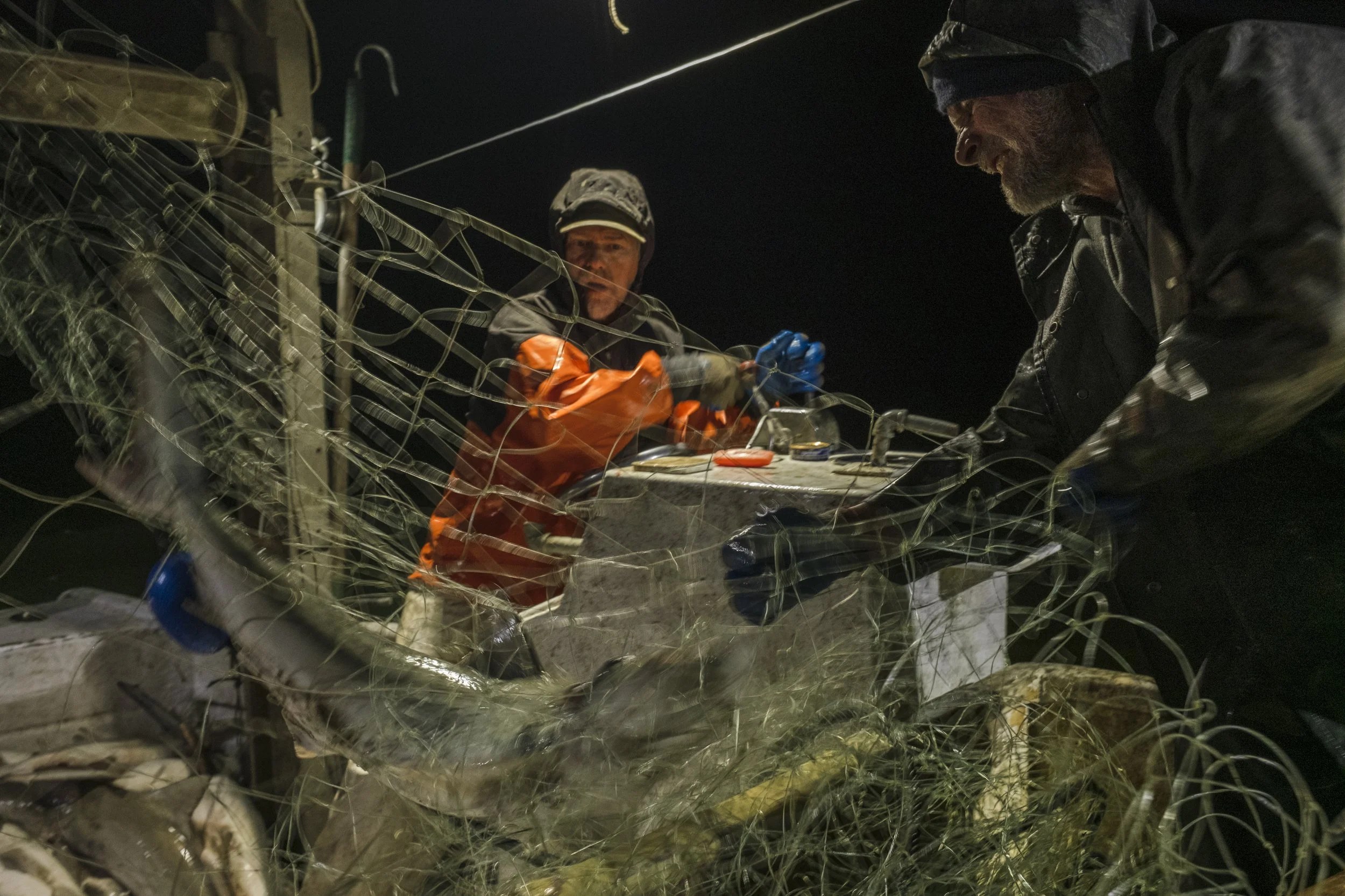 Two rescue workers in dark clothing and gloves work at night on a damaged vehicle entangled in a lot of broken barbed wire.
