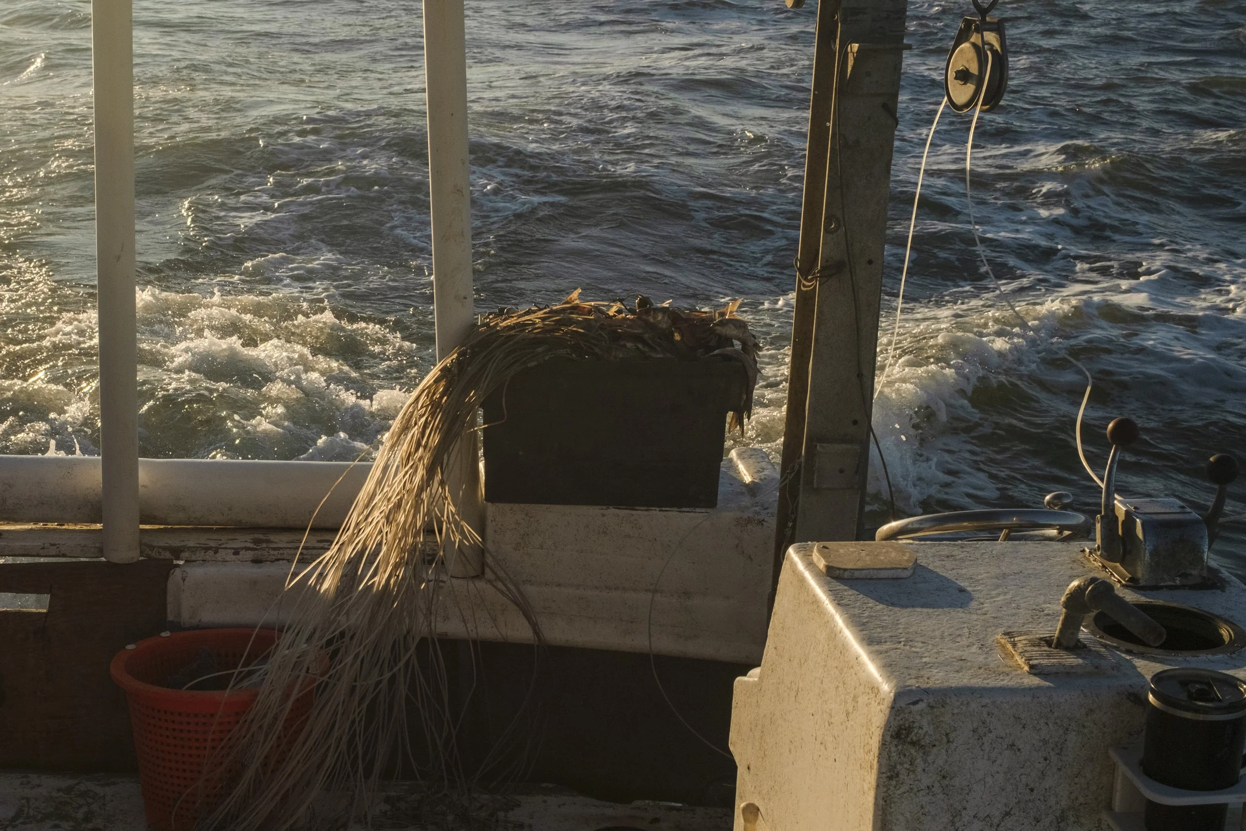 A view from a boat showing the ocean waves and part of the boat's control area with a black container filled with tangled fishing nets, a red basket, and various controls and wires.