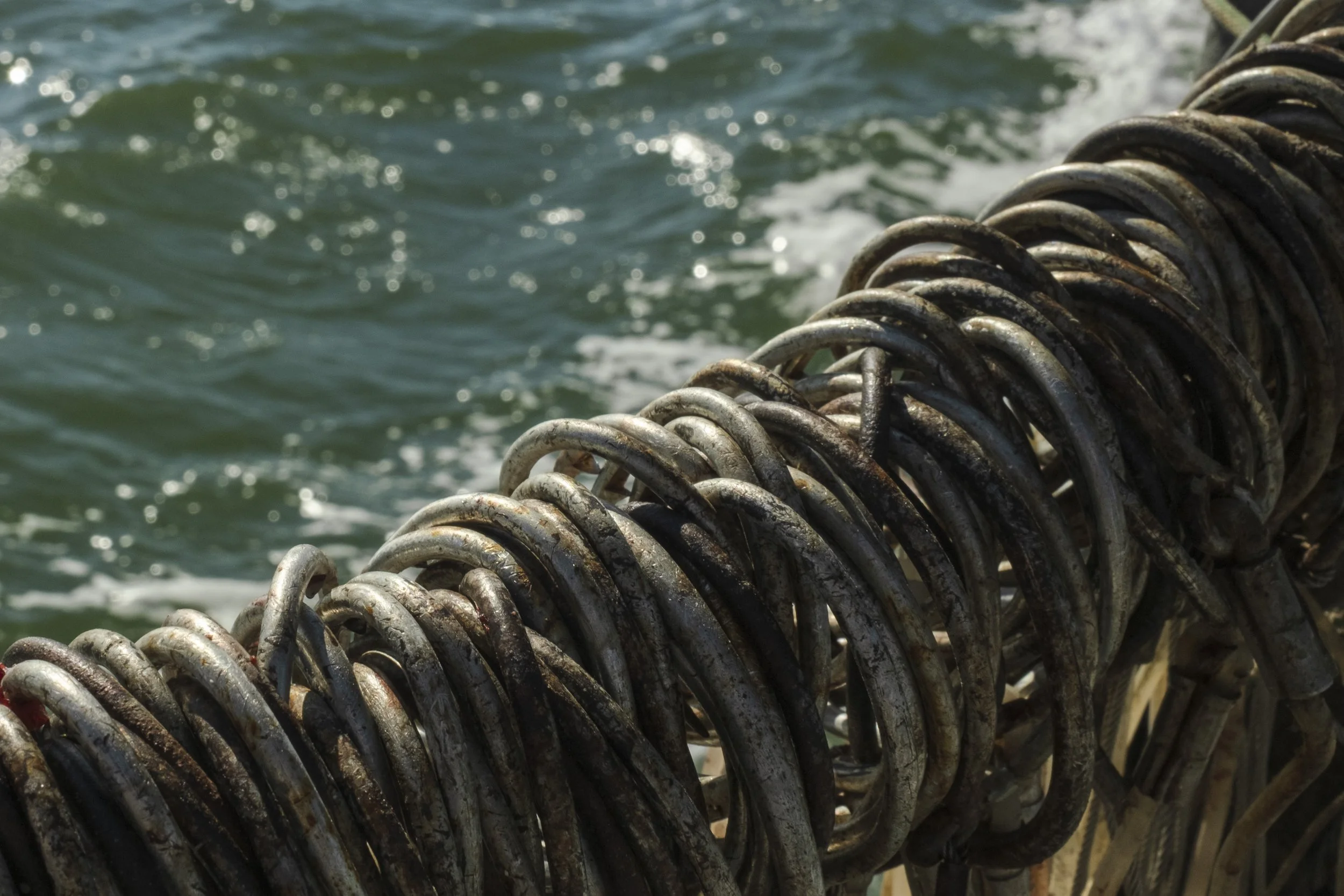 Close-up of rusty metal hooks attached to a wharf, with water in the background.
