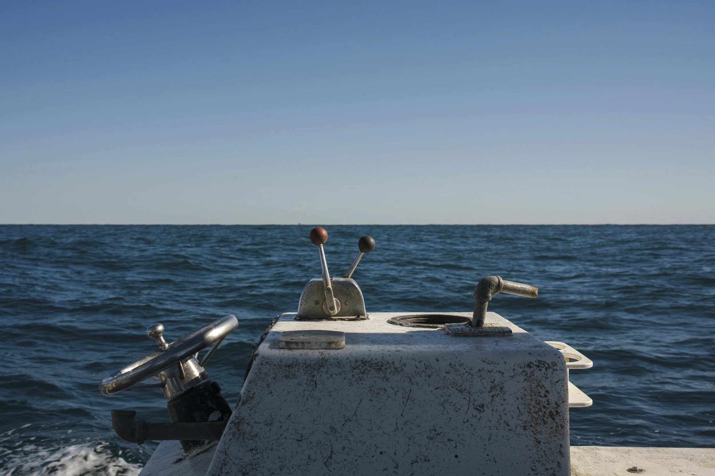 View from a boat showing the ocean with a clear blue sky and a navigation or control panel with metal levers and a wheel.
