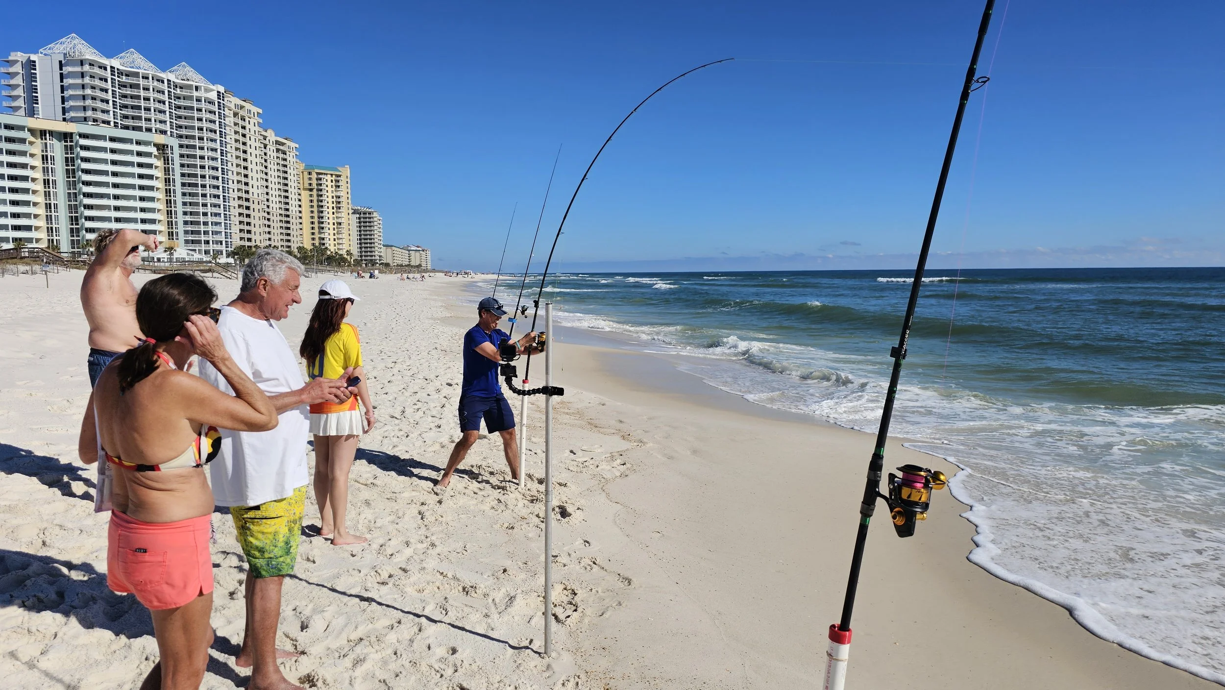 People fishing on the beach with high-rise buildings in the background on a sunny day.