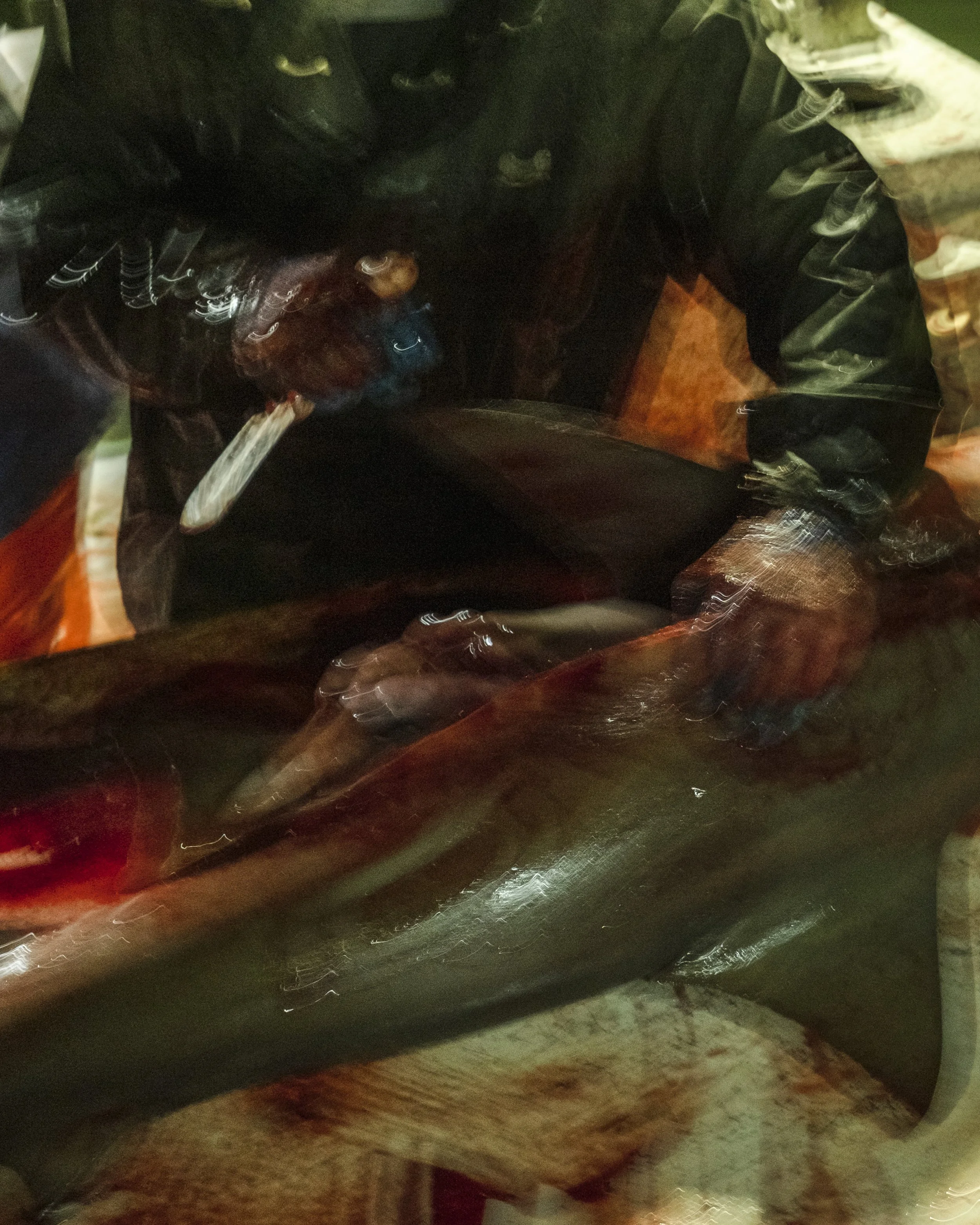 A person in waterproof clothing is handling a large fish, possibly at a fish market or fishing dock.