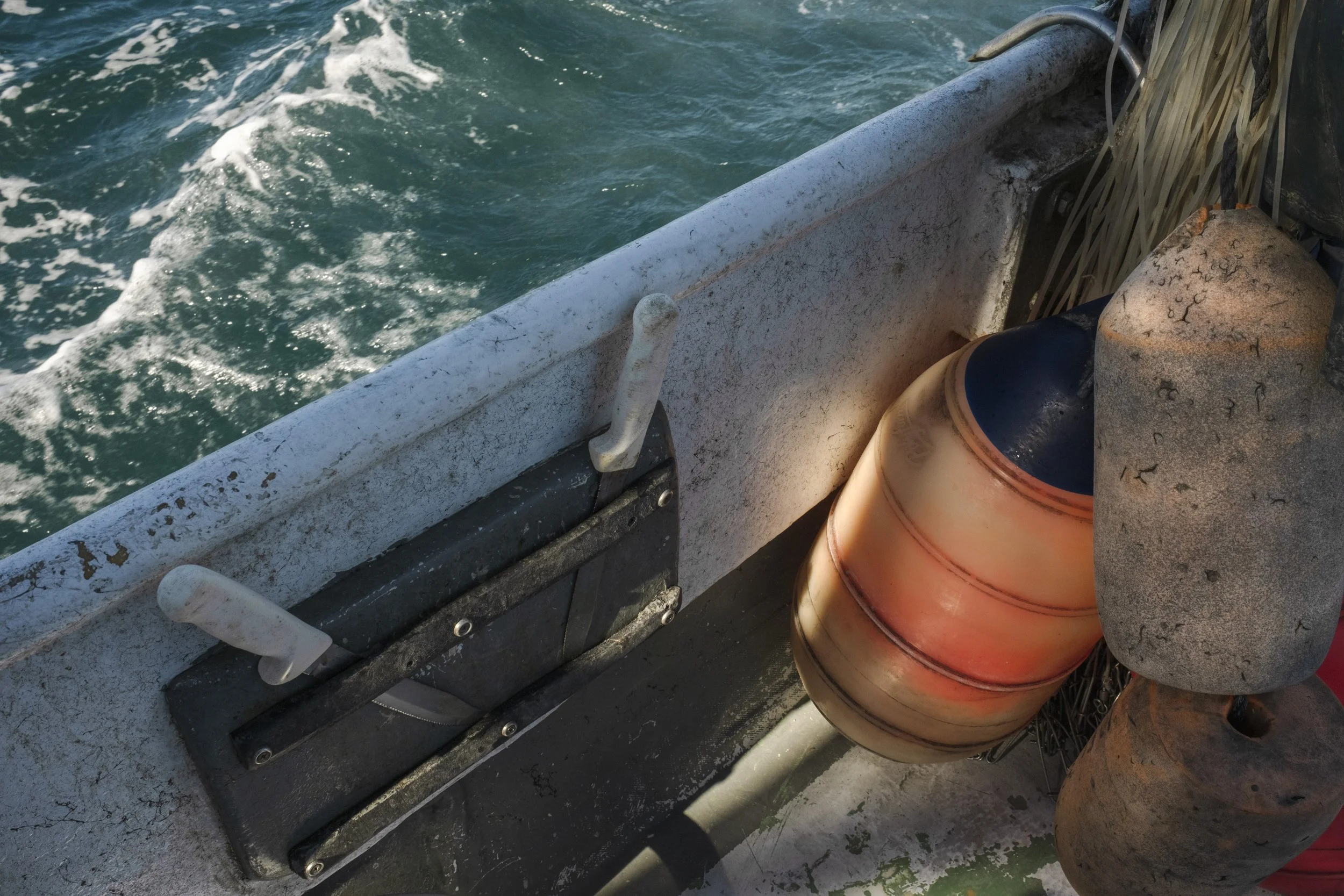 Close-up of a boat's edge with a buoy and two fenders, with water visible in the background.