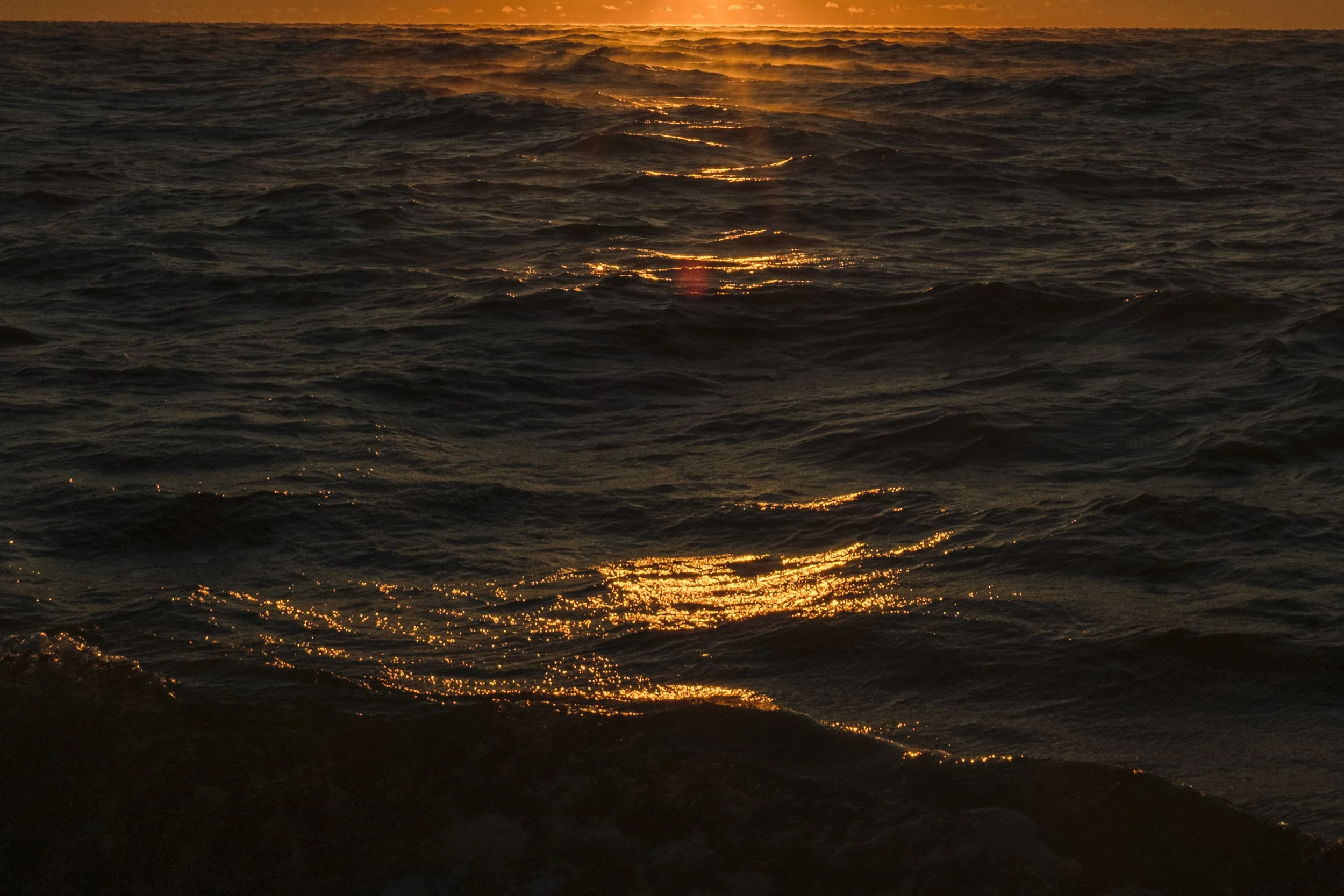 Sunset over dark ocean waves with golden reflections on the water surface.