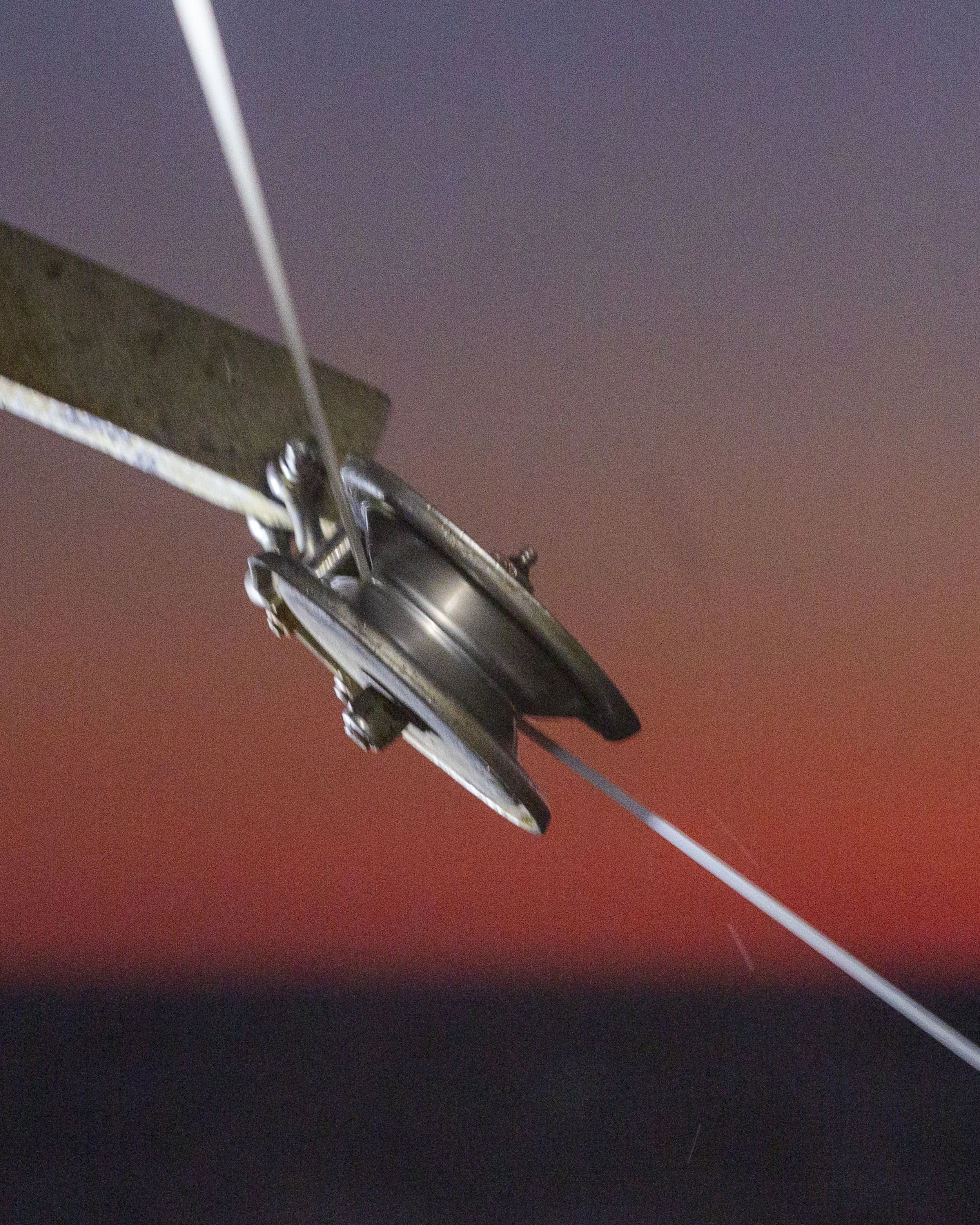 Close-up of a pulley system with metal components and a cable, against a gradient sky background.