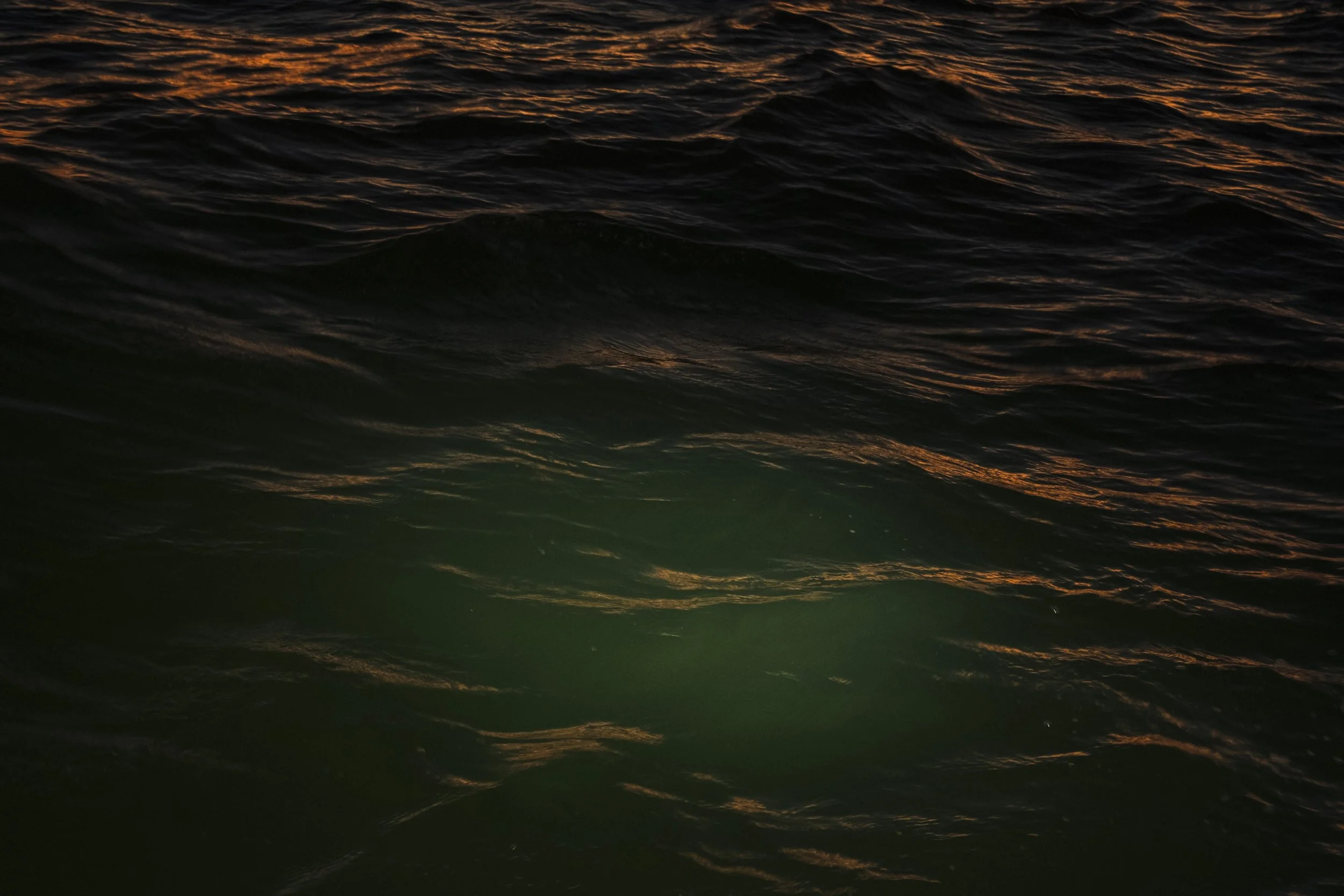Dark ocean water with gentle waves and reflections from the sunset.