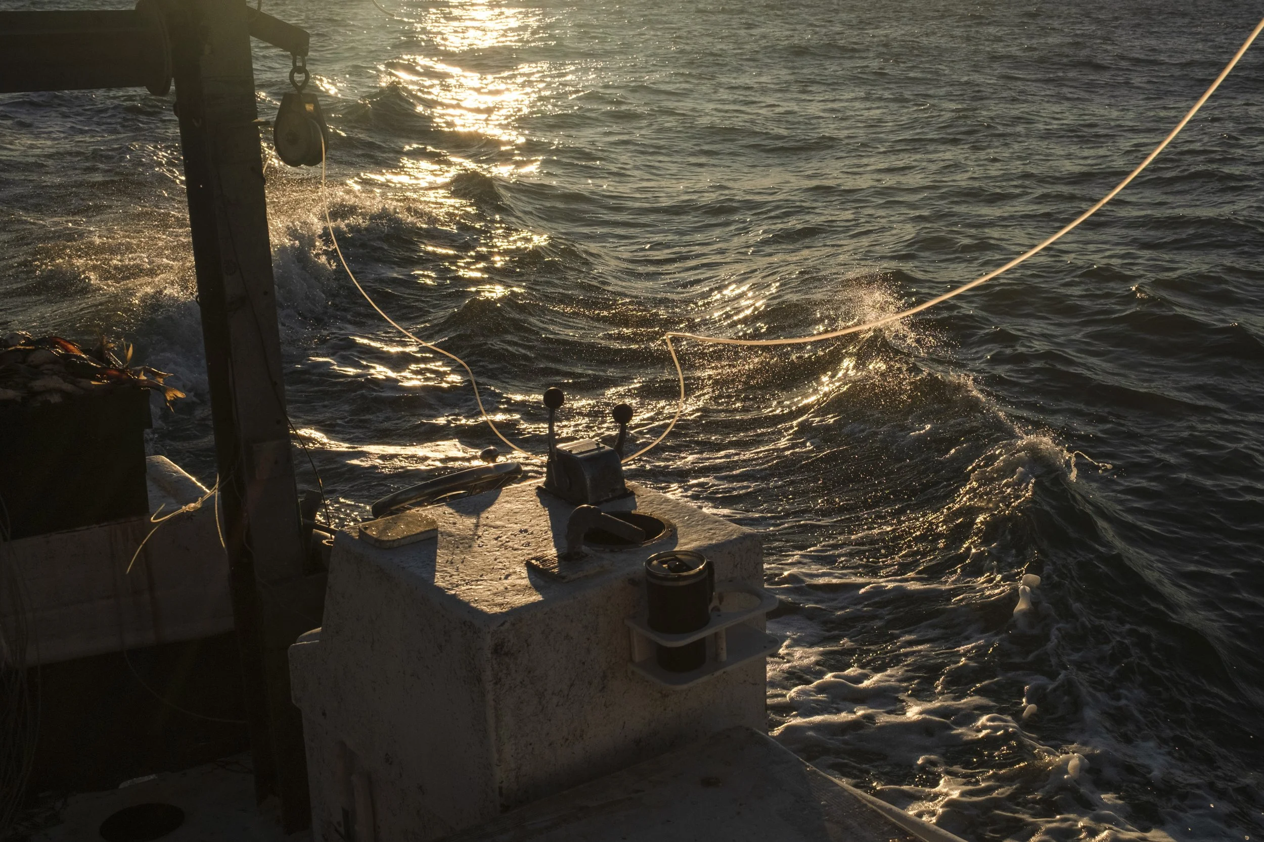 A view from a boat showing the ocean with sunlight reflecting off the water and a boat's console with various equipment and a rope secured to the boat.